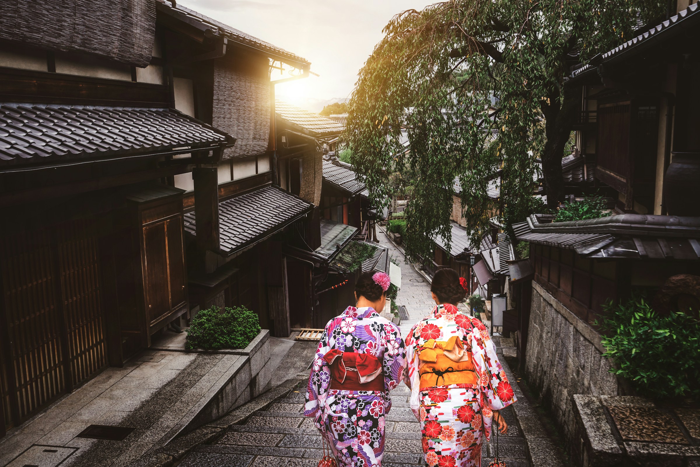 Two Japanese women in colorful dresses walking among Japanese buildings with sunset in the background