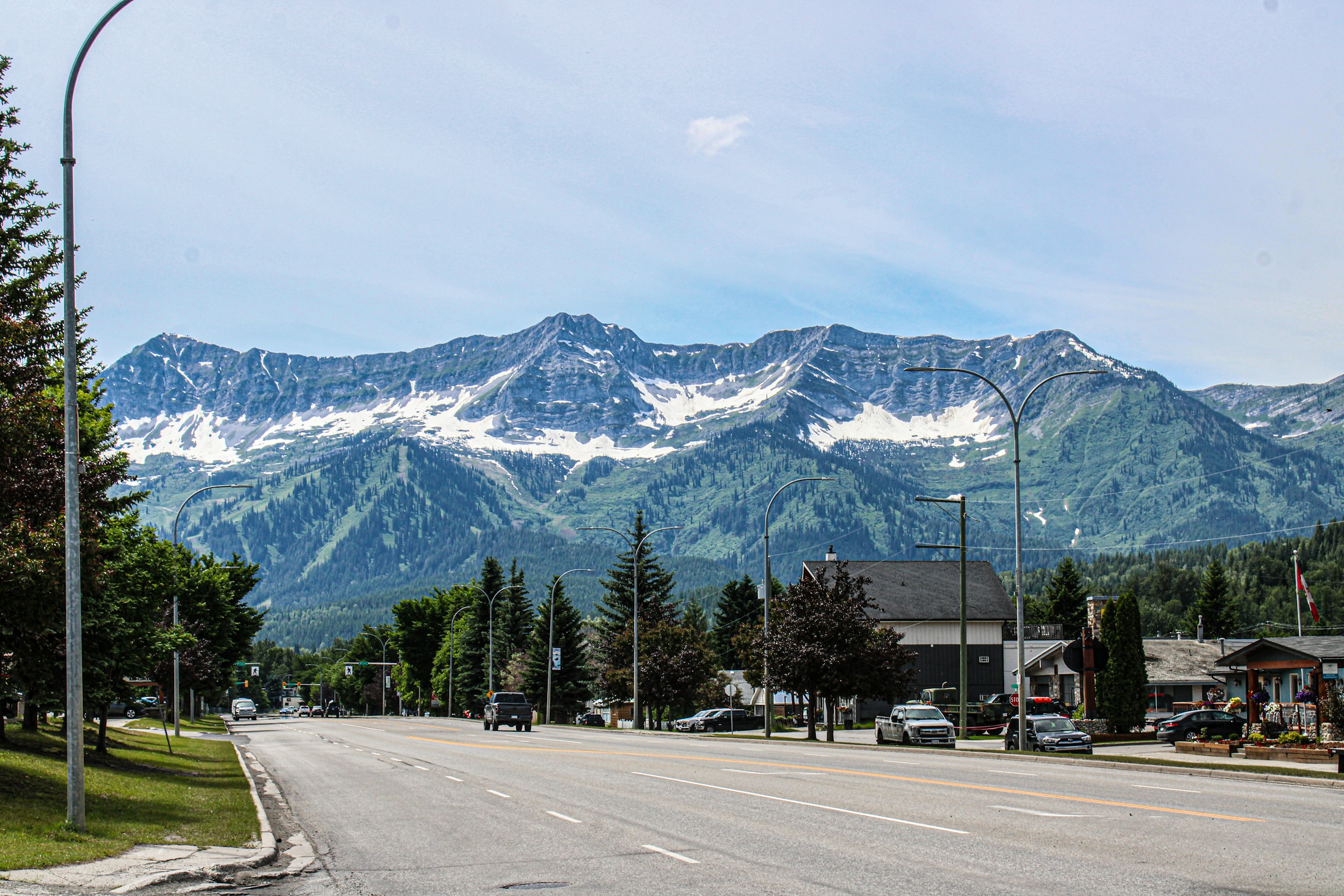 Stadsgata med vy över snöklädda bergstoppar och gröna sluttningar under en klarblå himmel i Fernie, Kanada.