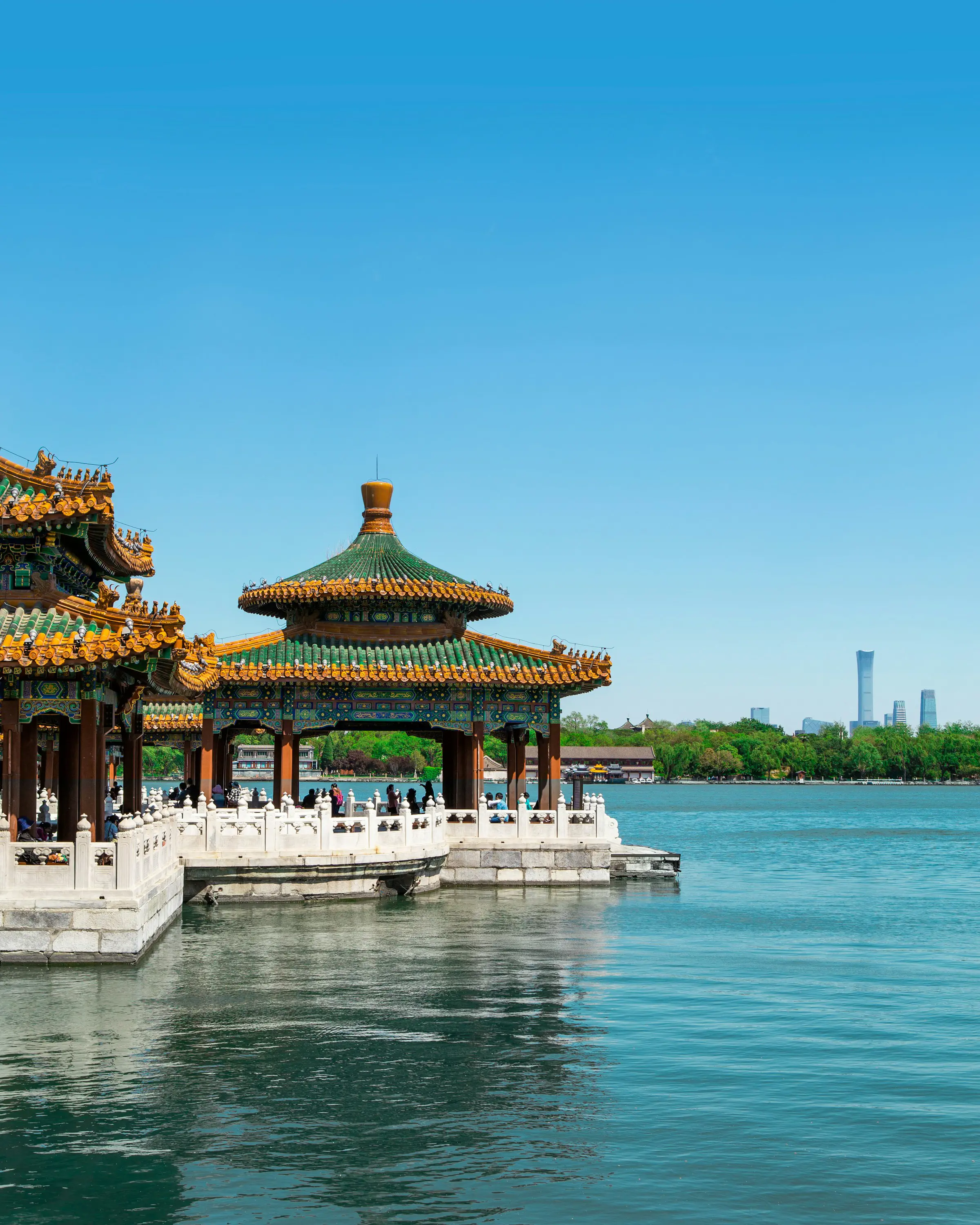 Klassiskt kinesiskt tempel i mindre storlek nere vid vattnet med Beijing storstad i bakgrunden