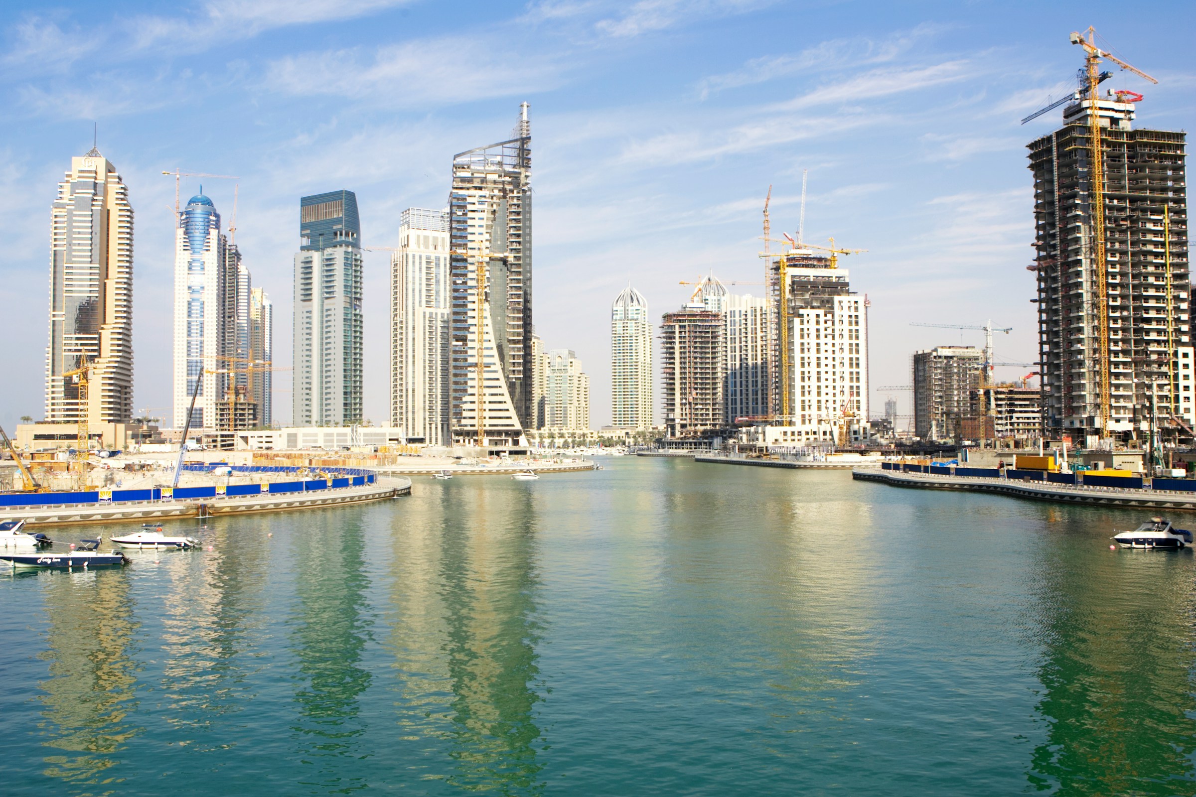 Skyline with high-rise buildings and construction cranes reflecting on the water, capturing the city's modern architecture and urban development.