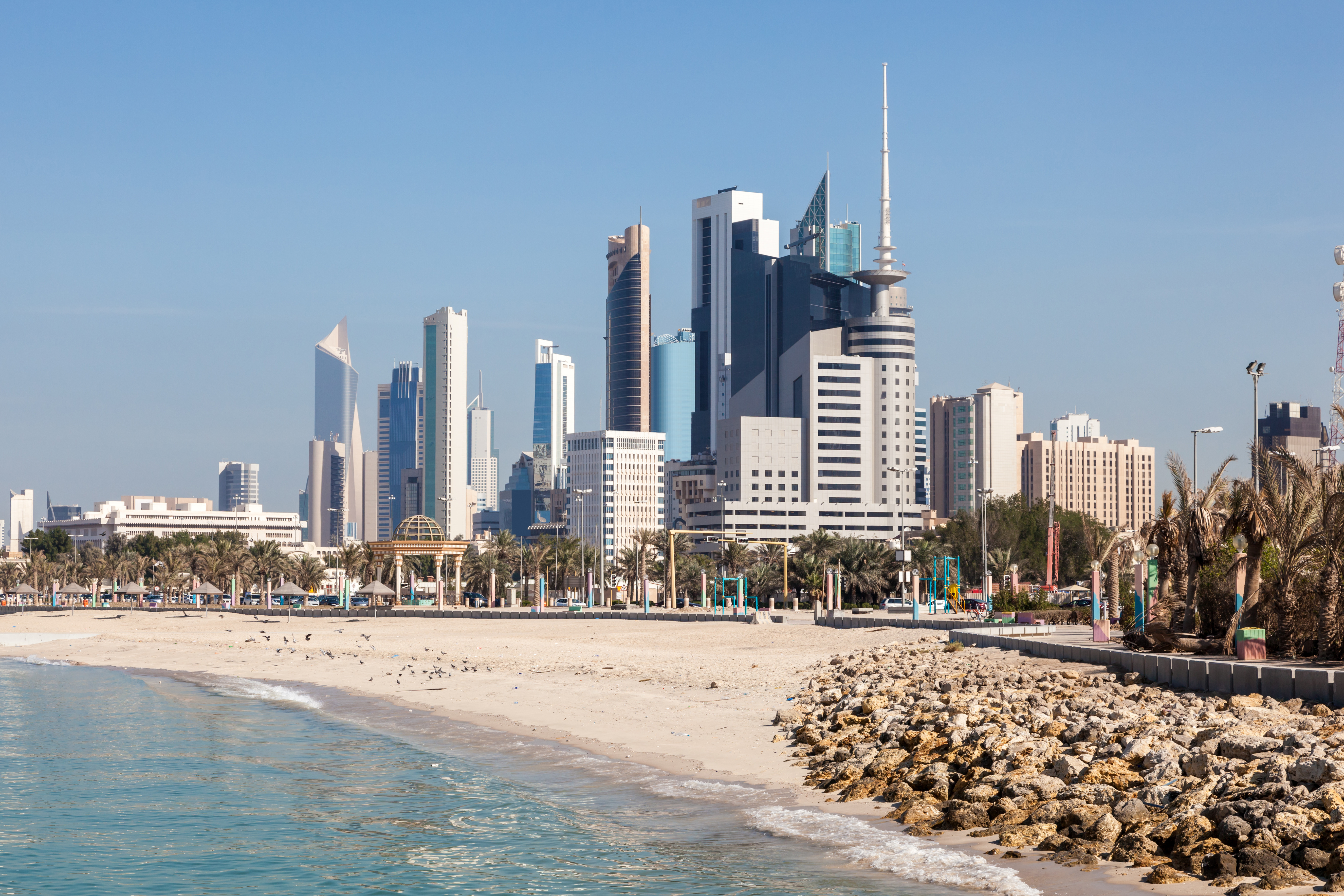 Travel to Kuwait - Kuwait City with modern skyscrapers along the beach, featuring clear blue water and a sandy shore.