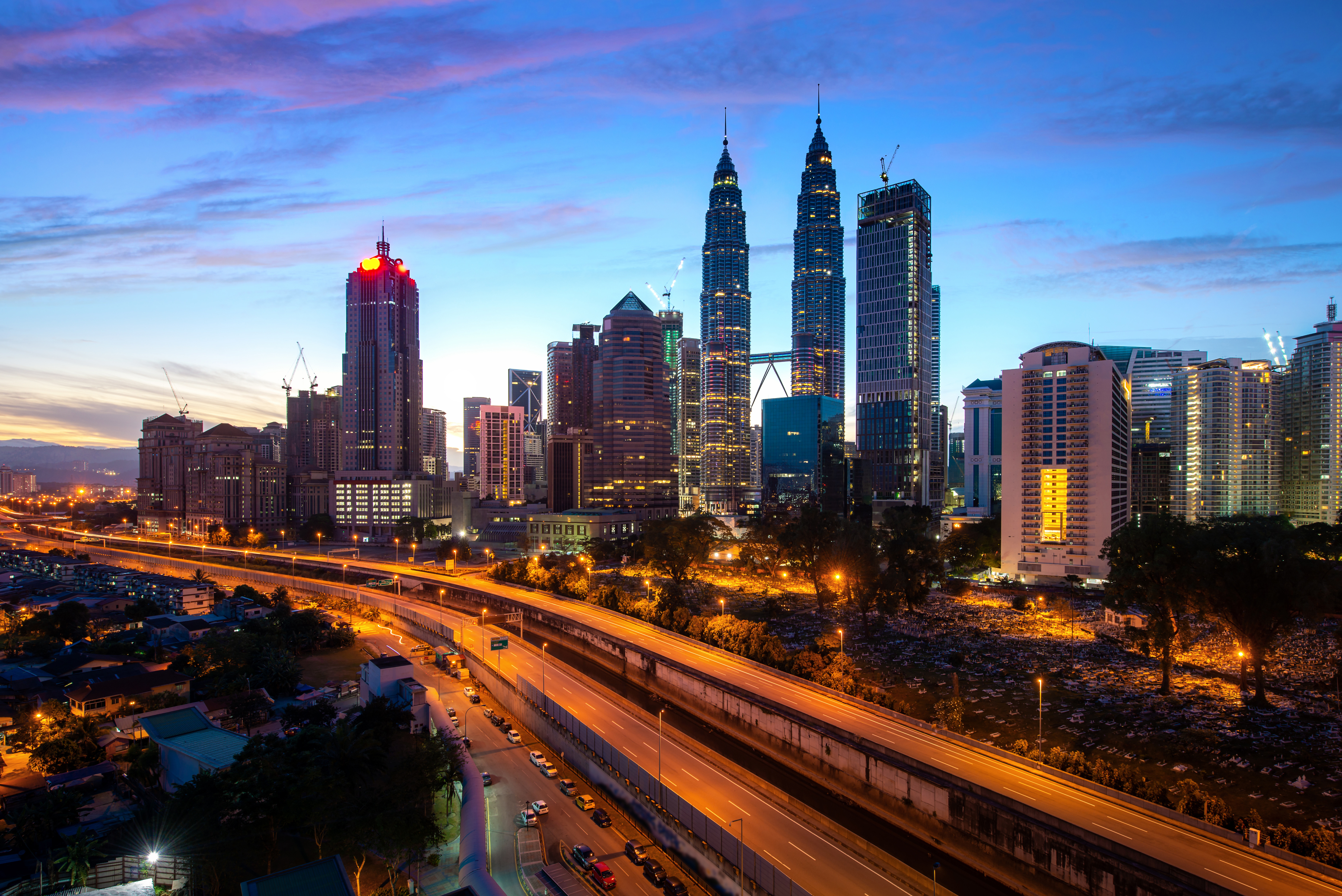 Kuala Lumpur city skyline at dusk featuring the Petronas Twin Towers, illuminated with vibrant city lights and a clear evening sky