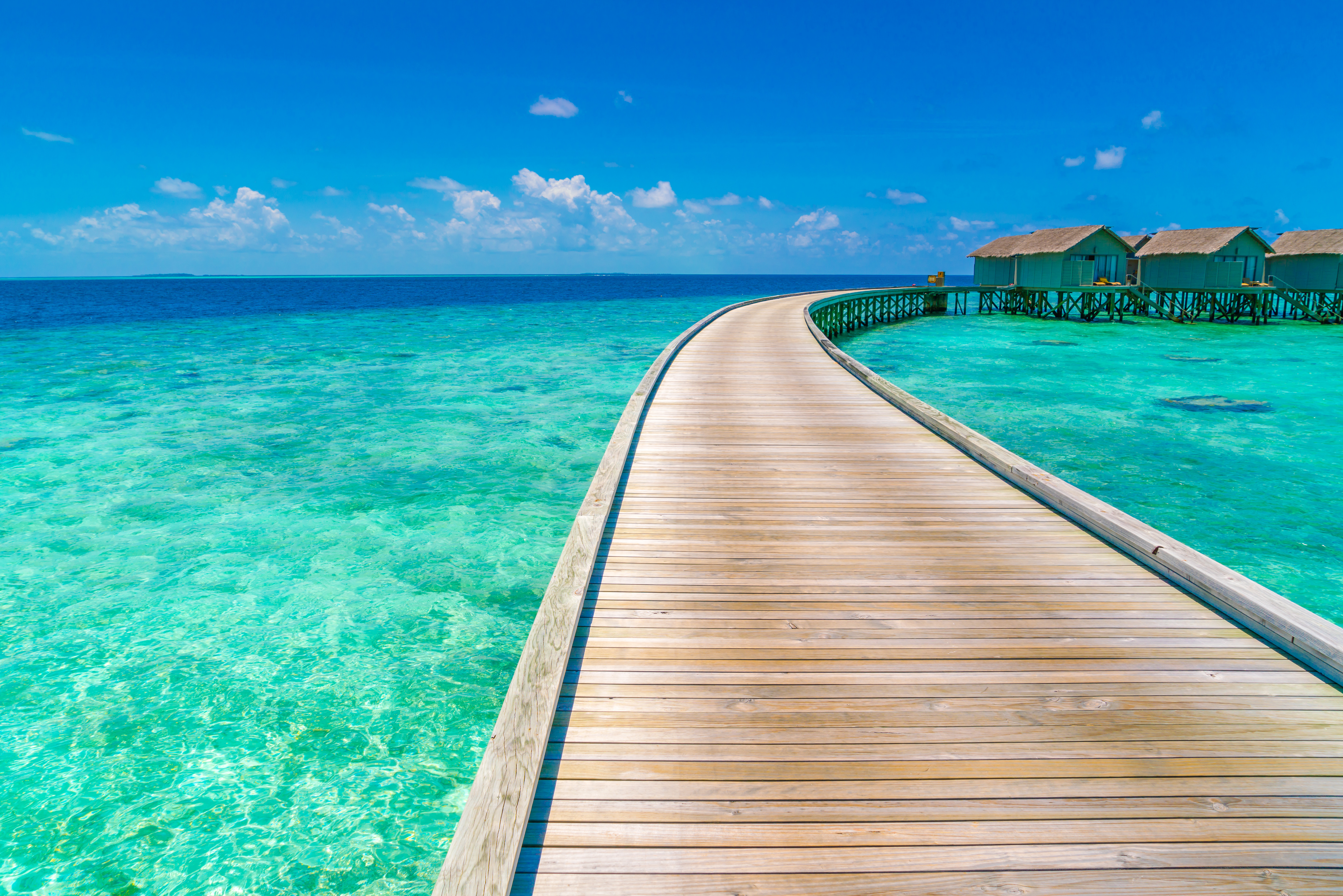 Wooden boardwalk leading to overwater bungalows on turquoise ocean under clear blue sky