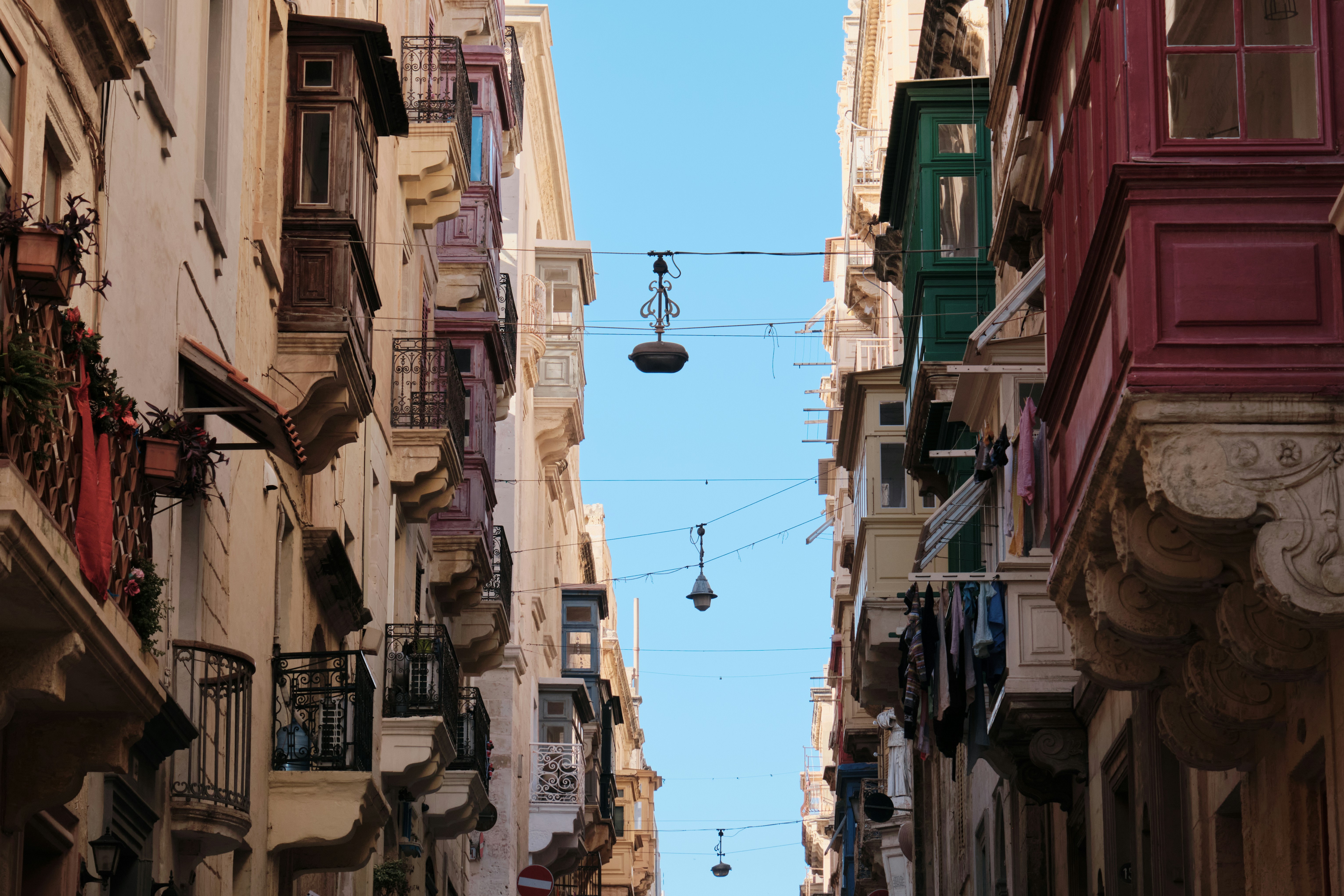 Narrow street with traditional Maltese balconies under a clear blue sky in Valletta, Malta