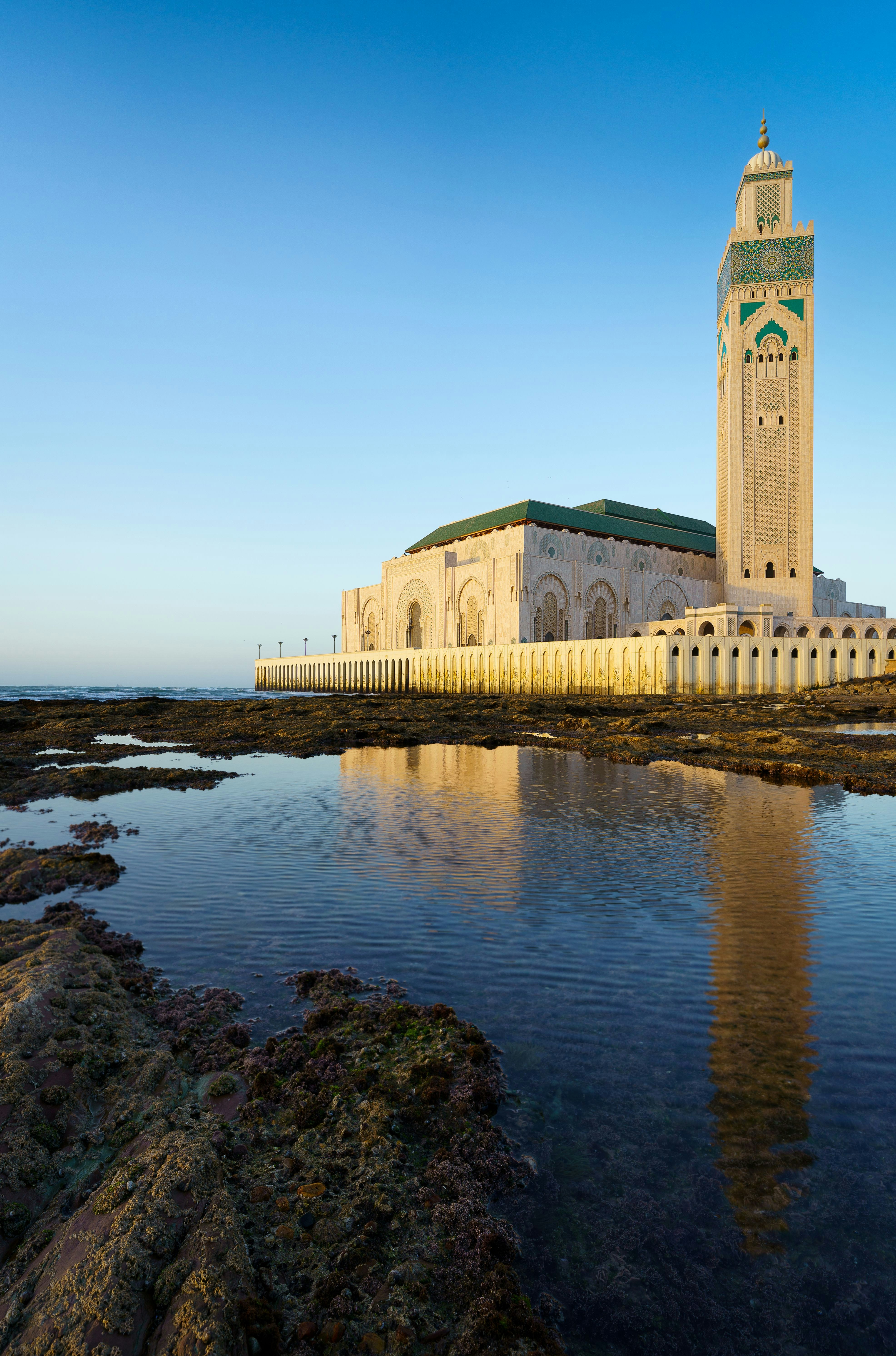 Hassan II Mosque in Casablanca, Morocco, reflected in calm coastal waters under a clear blue sky