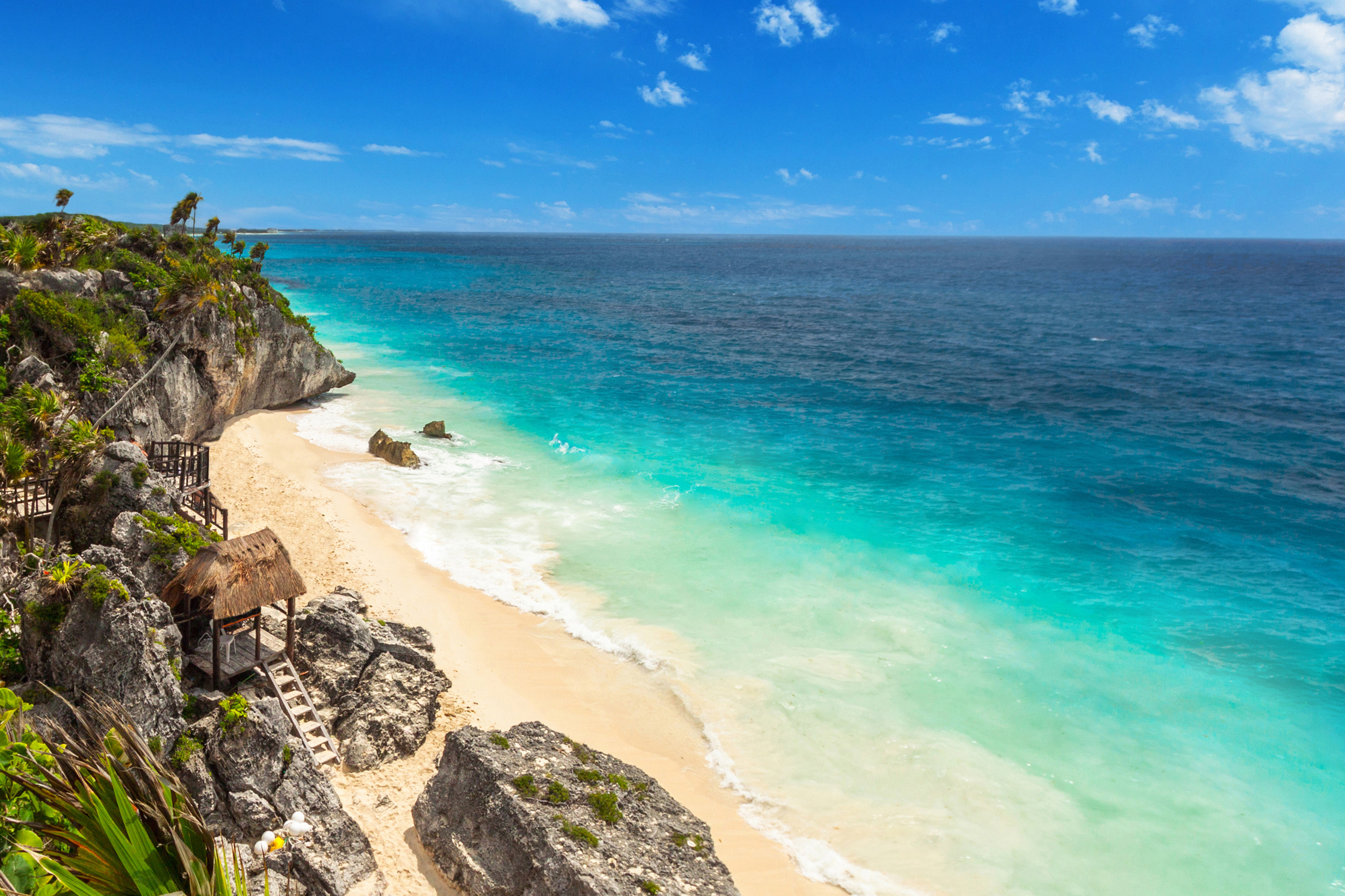 Tropical beach with turquoise waters, white sand, and rocky cliffs under a clear blue sky