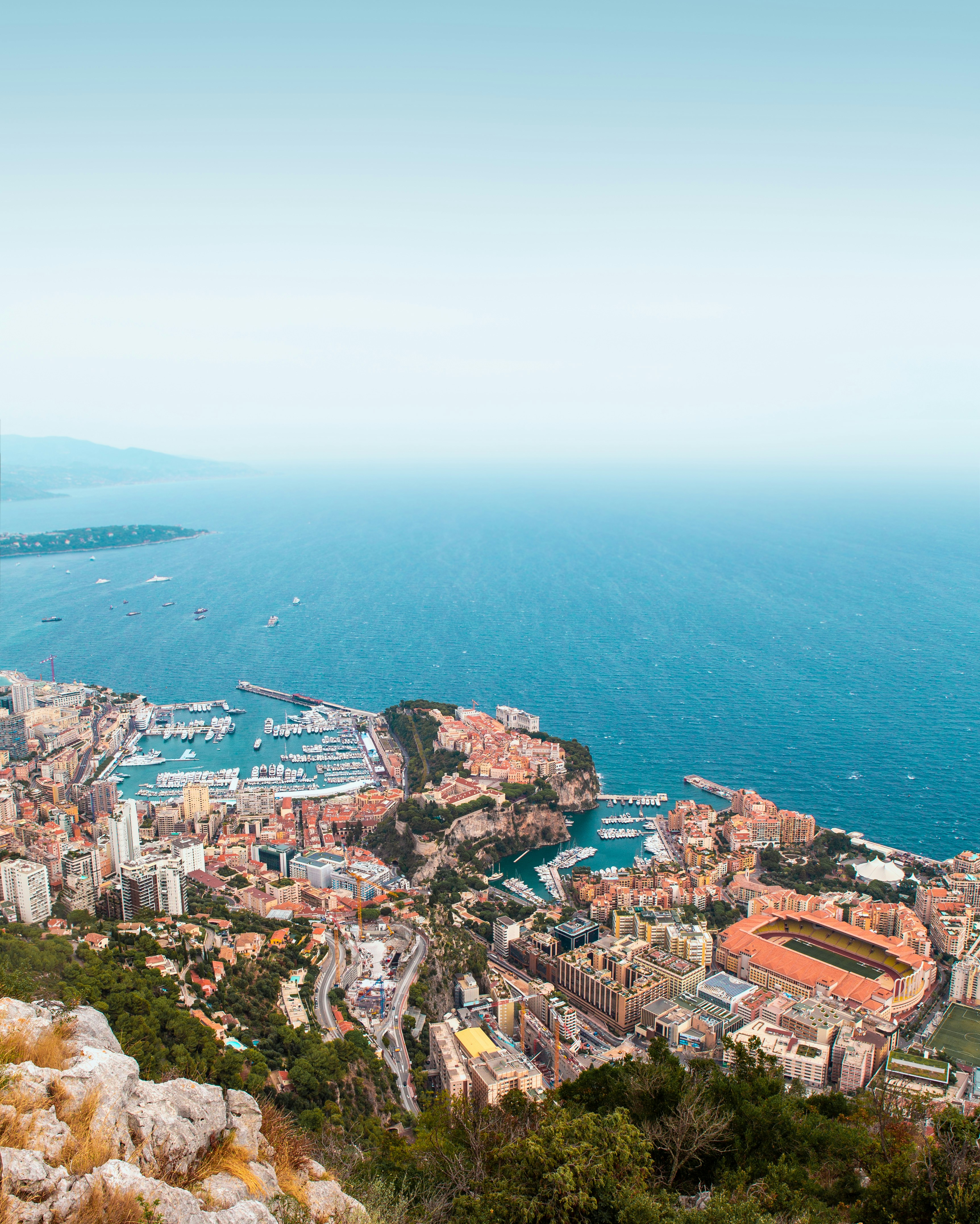 Aerial view of Monaco coastline featuring Monte Carlo skyline, harbor with yachts, and Mediterranean Sea