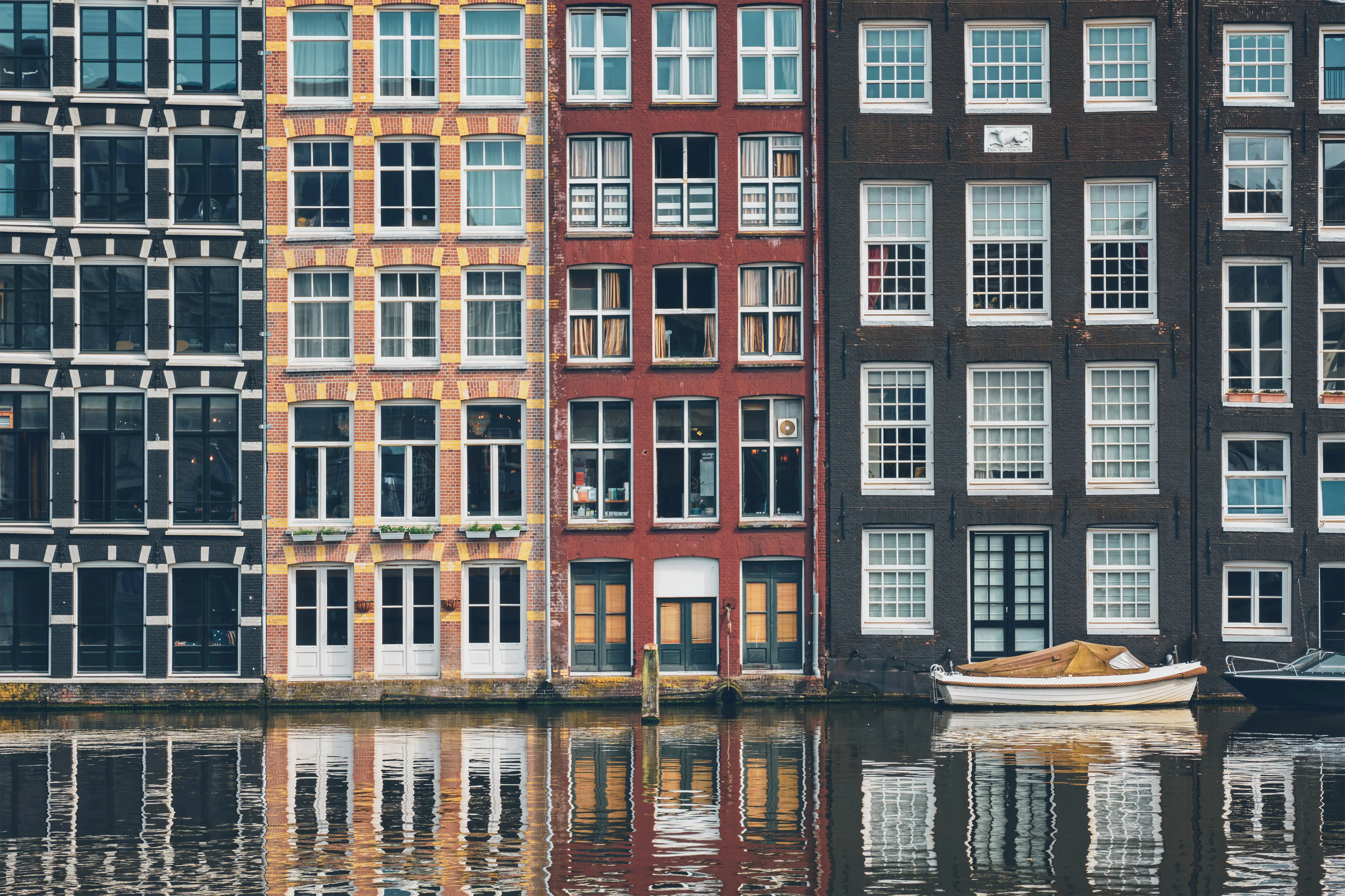 Canal houses with colorful facades and large windows reflected in the water in Amsterdam