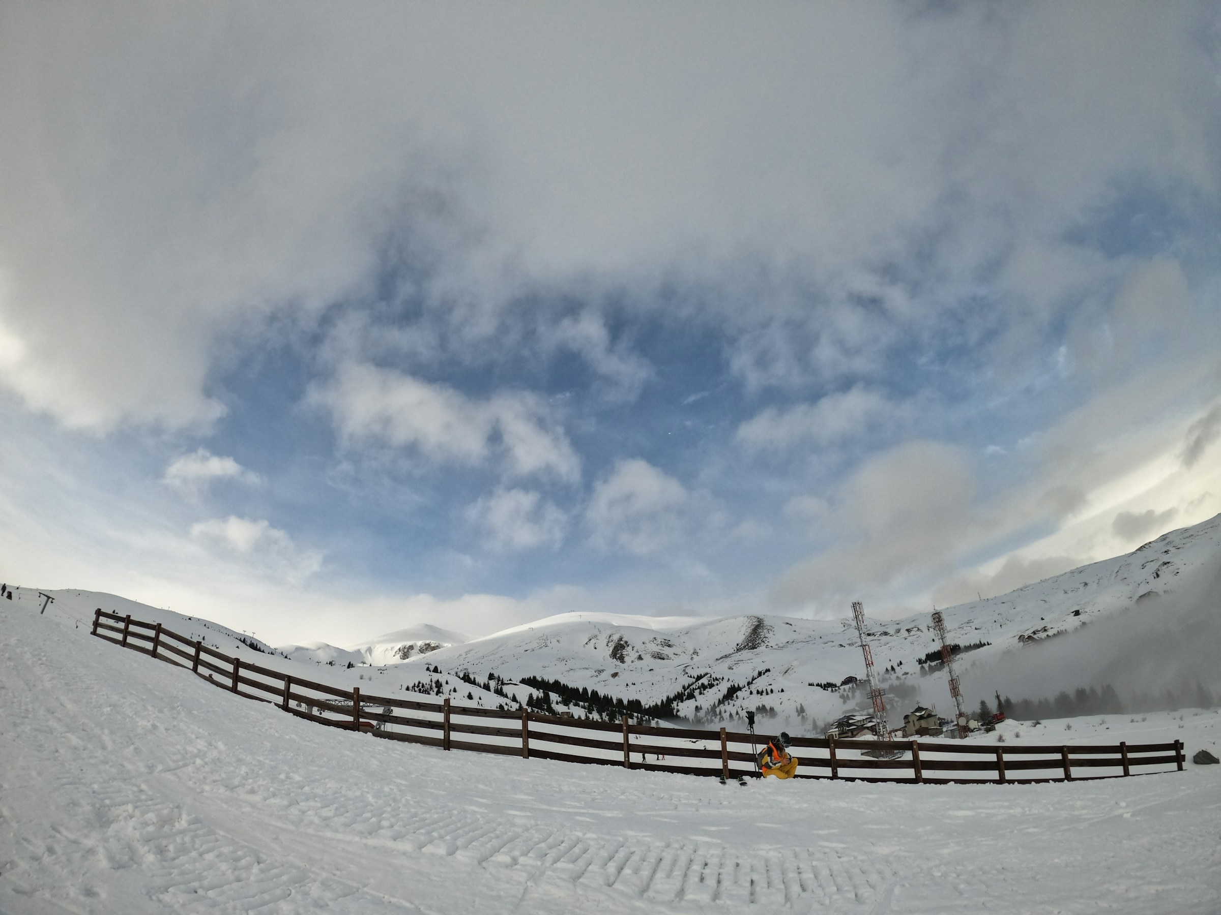 En snötäckt skidbacke med en delvis molnig himmel och berg i bakgrunden