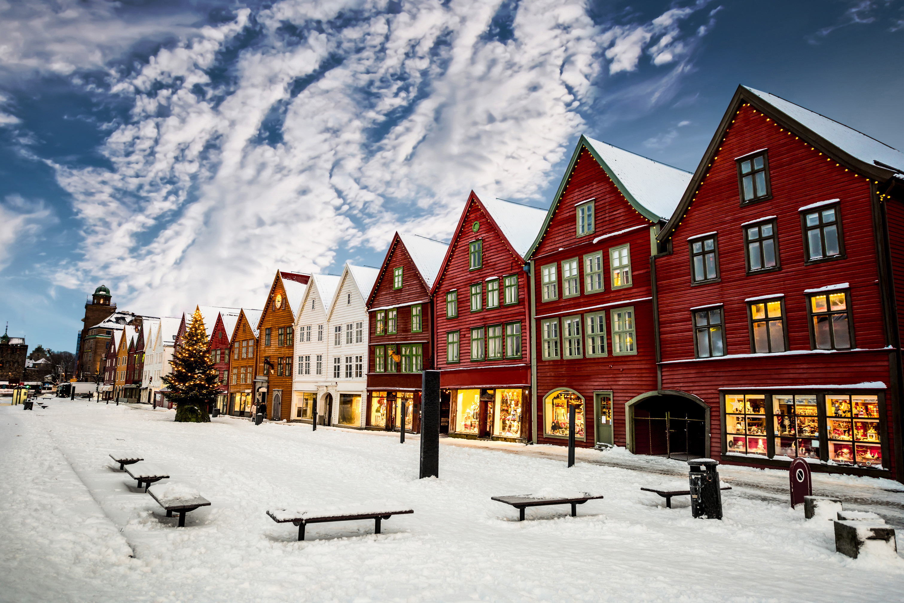 Colorful historic buildings in a snow-covered street under a cloudy sky, decorated with Christmas lights, Bryggen district, Bergen, Norway