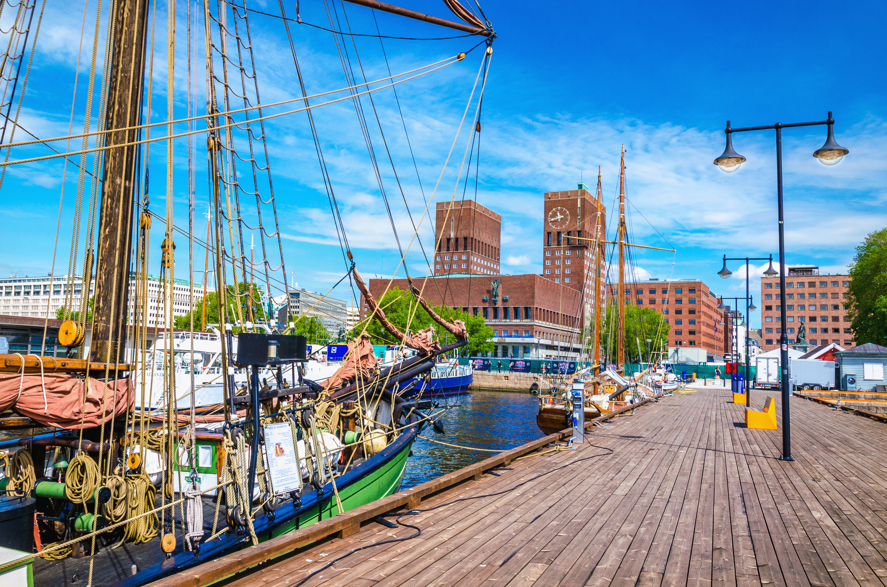 Historic ships docked at the pier with Oslo City Hall in the background, set against a bright blue sky