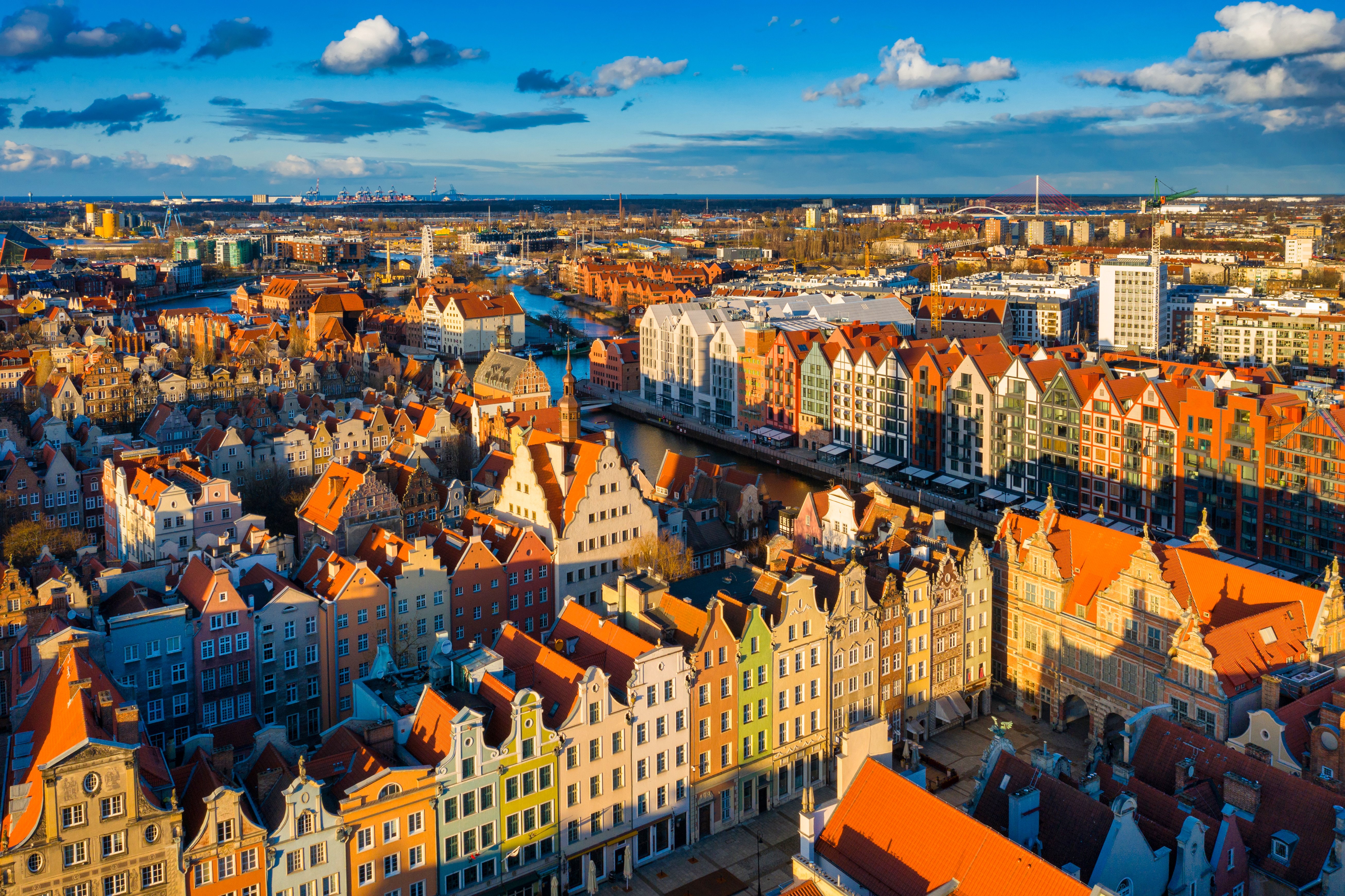Aerial view of Gdańsk, Poland, showcasing colorful historic buildings and red rooftops under a clear blue sky, with the cityscape and harbor in the background