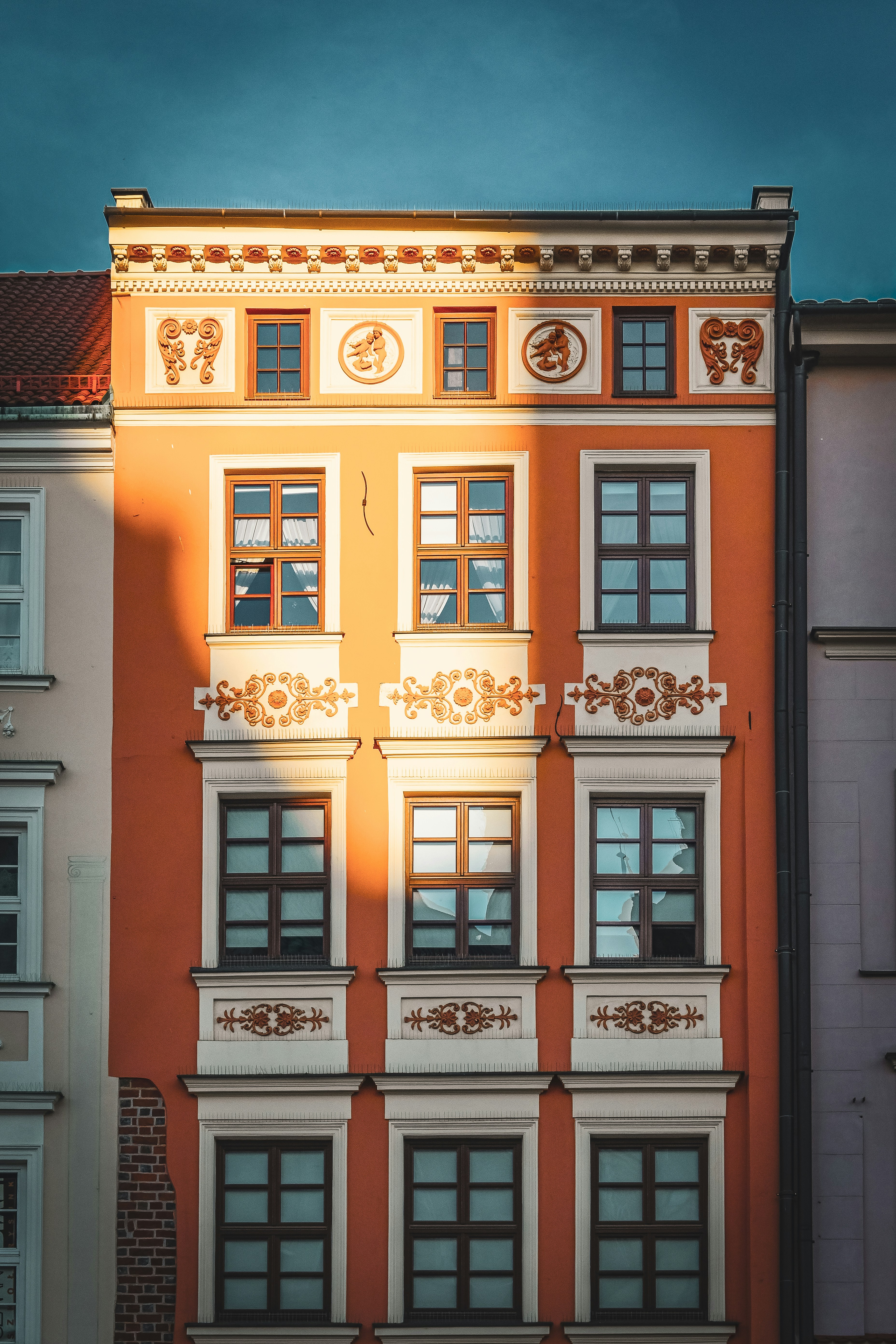 Ornate European townhouse facade with orange and cream detailing, featuring decorative moldings and framed windows under a clear blue sky
