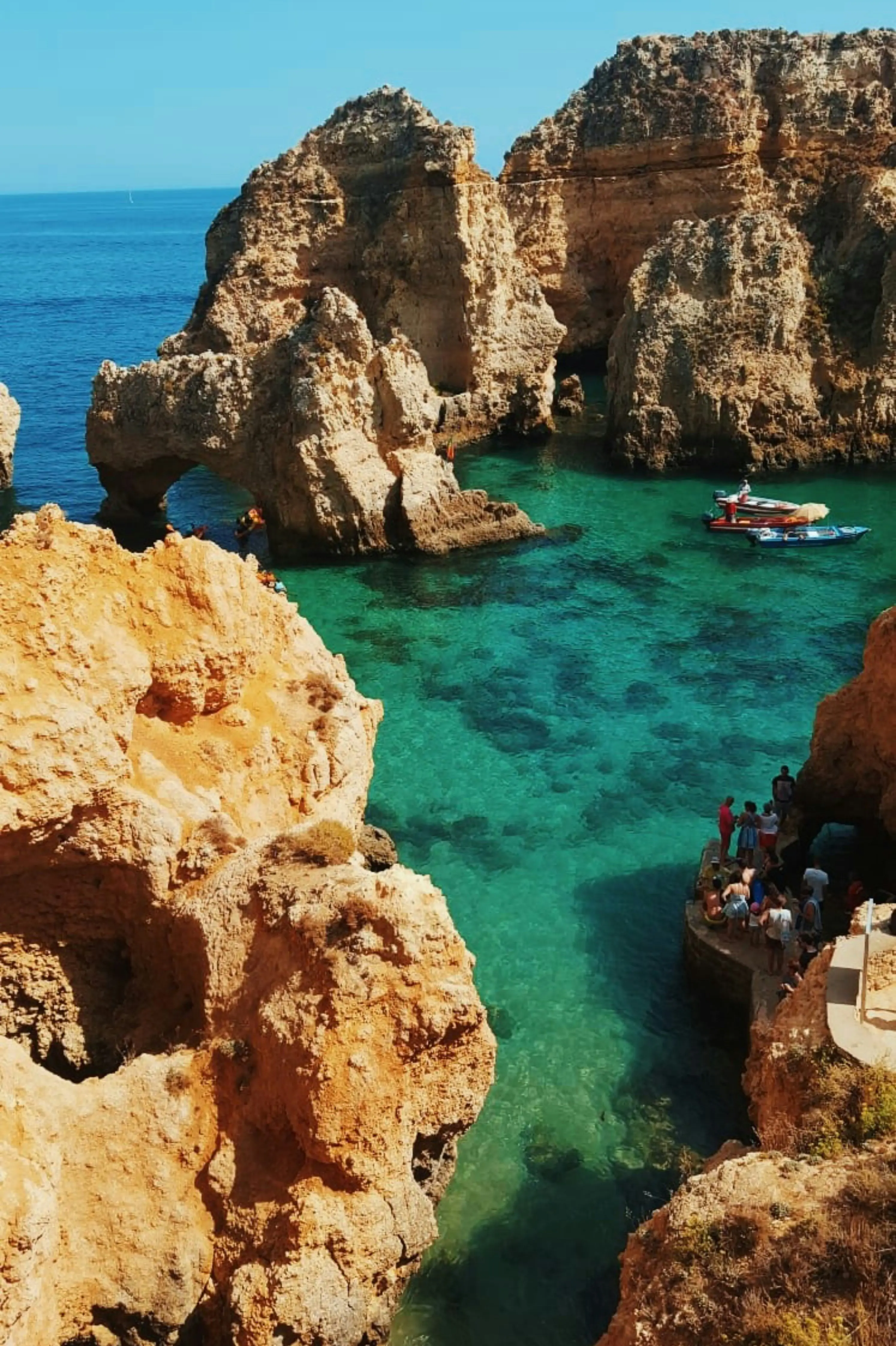 Scenic view of rocky cliffs and turquoise waters at Ponta da Piedade, Algarve, Portugal, with a boat and tourists exploring the natural formations