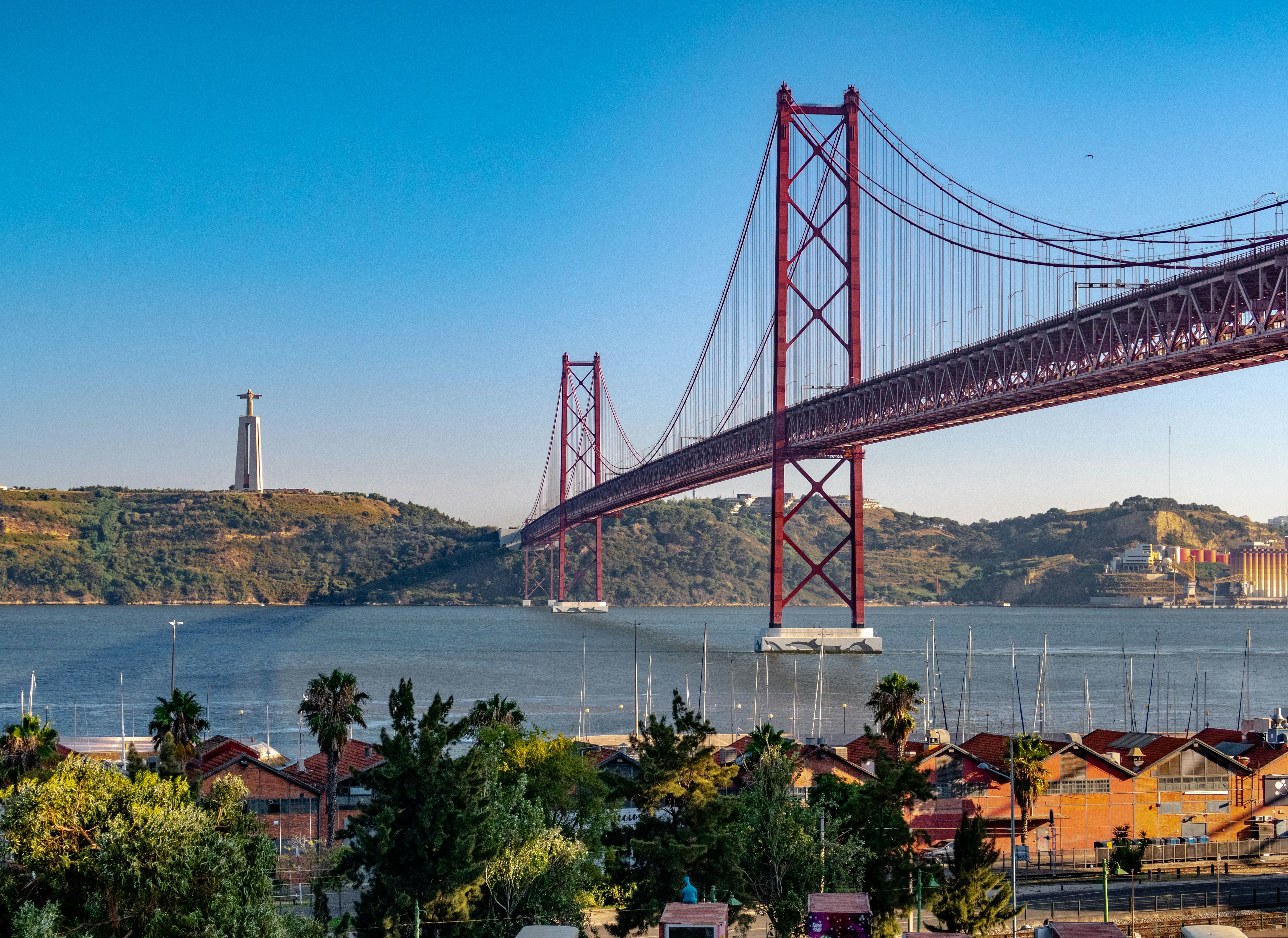 25 de Abril Bridge spanning the Tagus River in Lisbon, Portugal, with the Cristo Rei statue visible on the left, under a clear blue sky