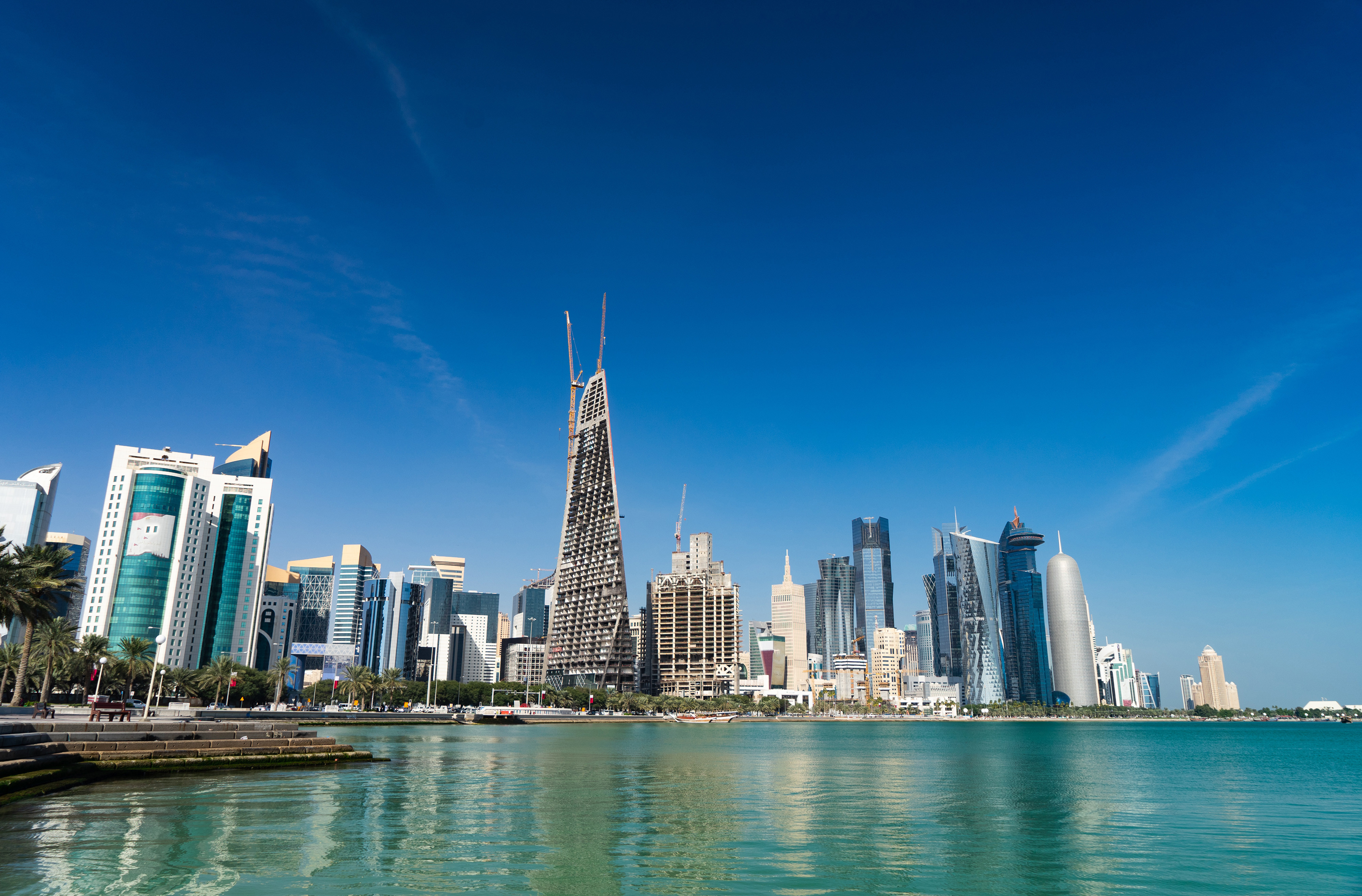 Doha skyline with modern skyscrapers and clear blue sky reflecting on the waterfront, showcasing Qatar's architectural development