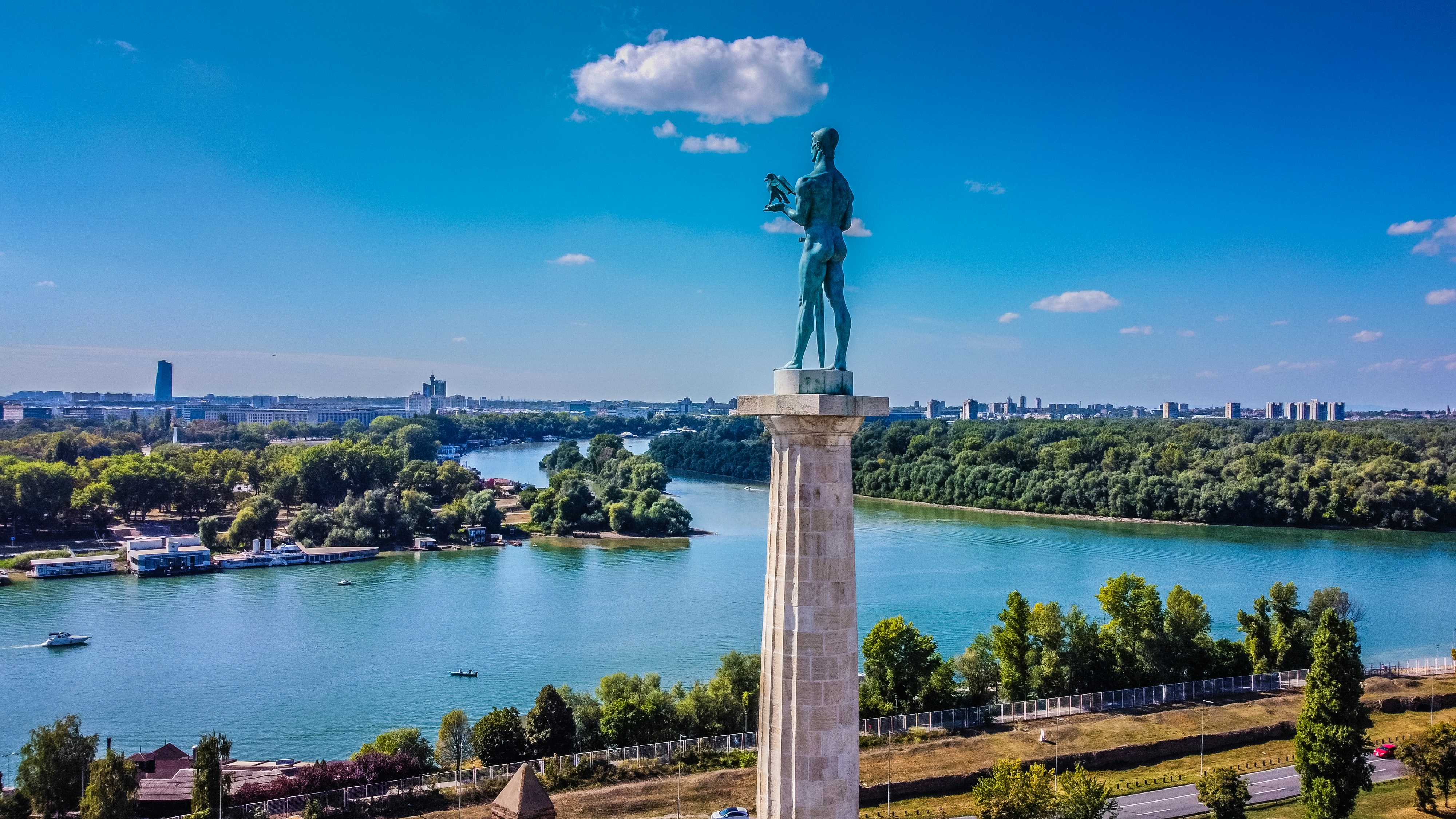 Statue of Pobednik overlooking rivers with city skyline in Belgrade, Serbia, under blue skies