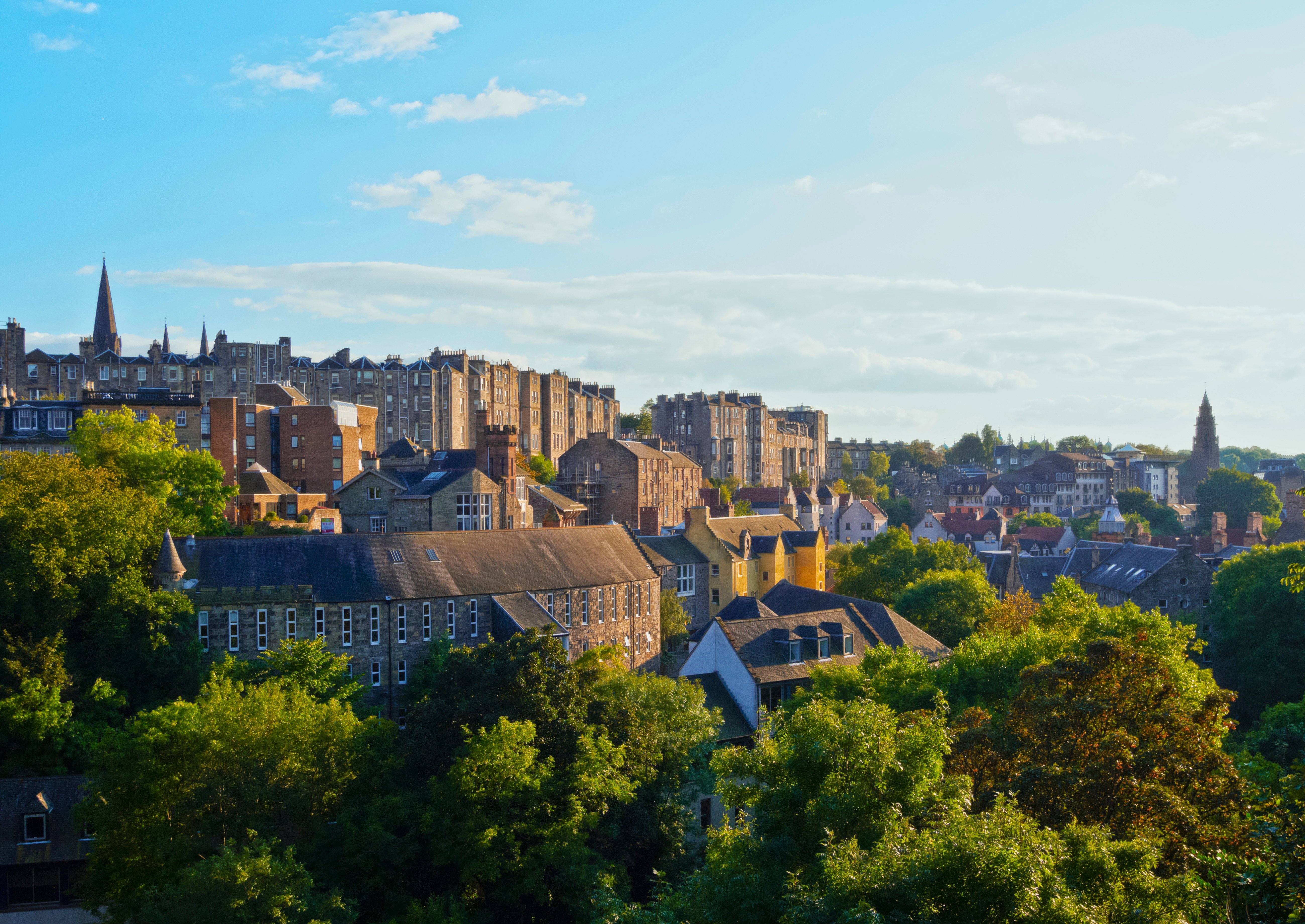 Travel to Edinburgh - Showcasing historic stone buildings and lush greenery under a bright blue sky.