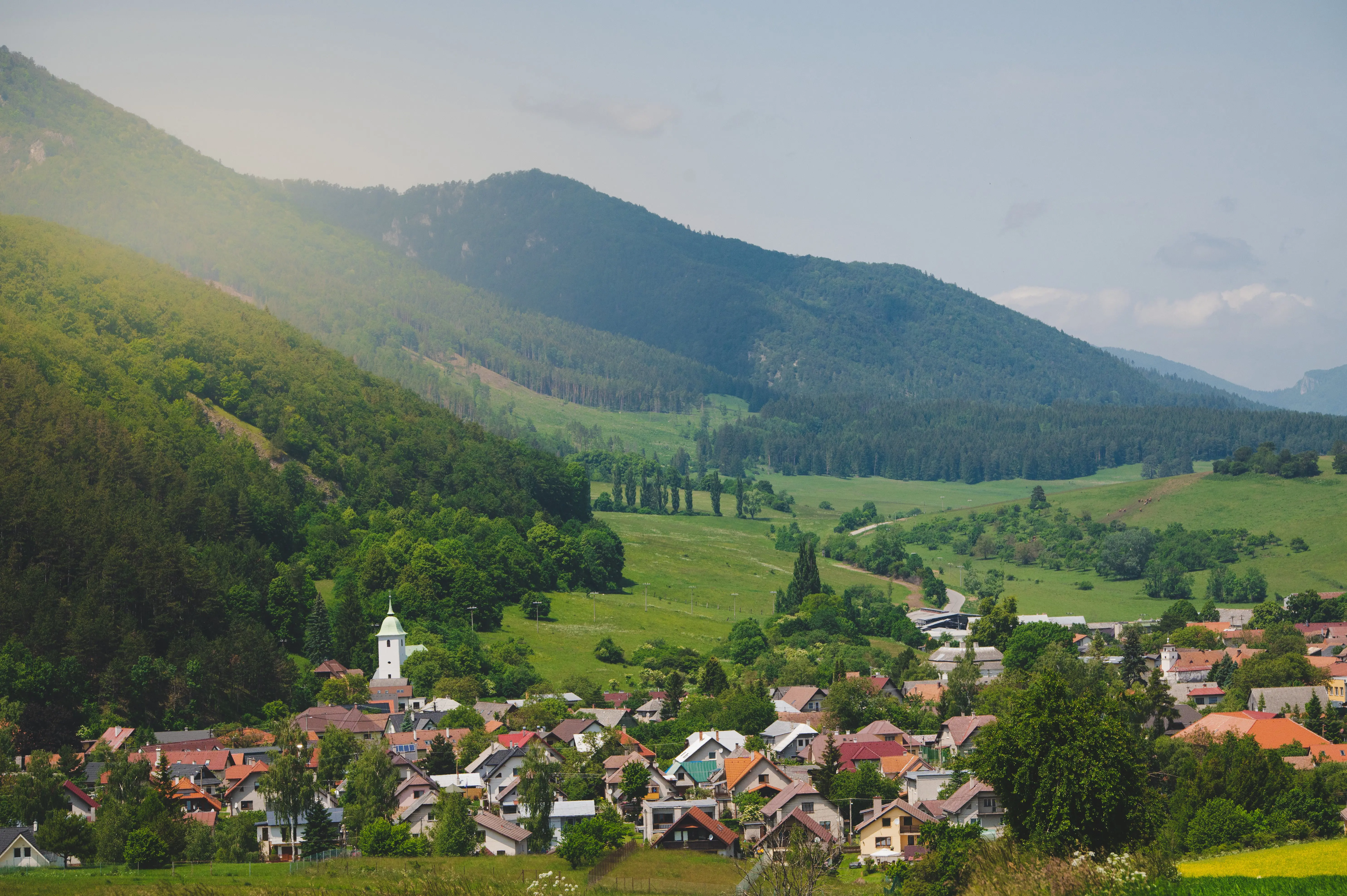 Utkant av stad i Slovakien med byggnader mot grönskande skog och berg med en soluppgång