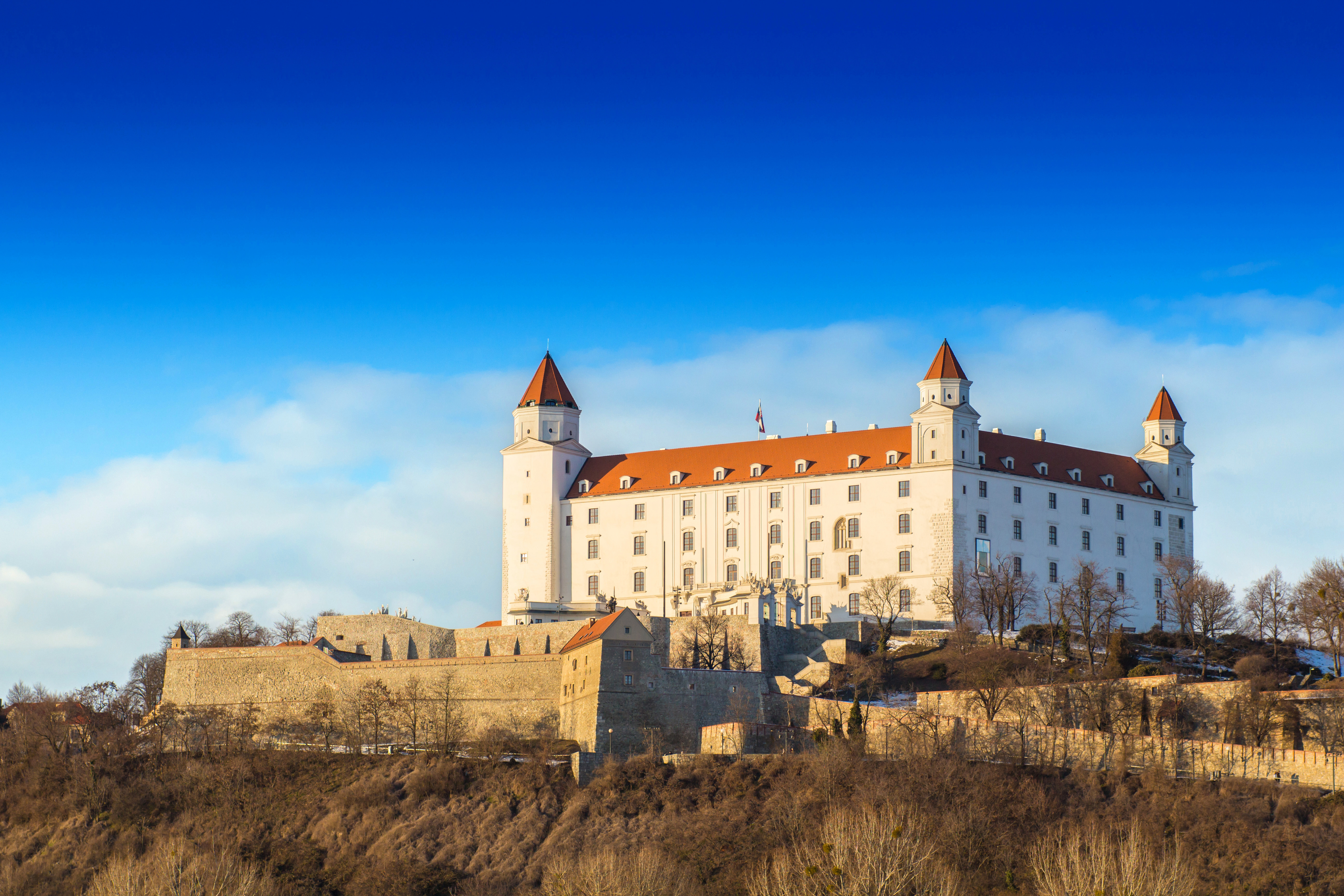 Bratislava Castle on a sunny day, featuring its distinct red roof and white facade, set against a clear blue sky