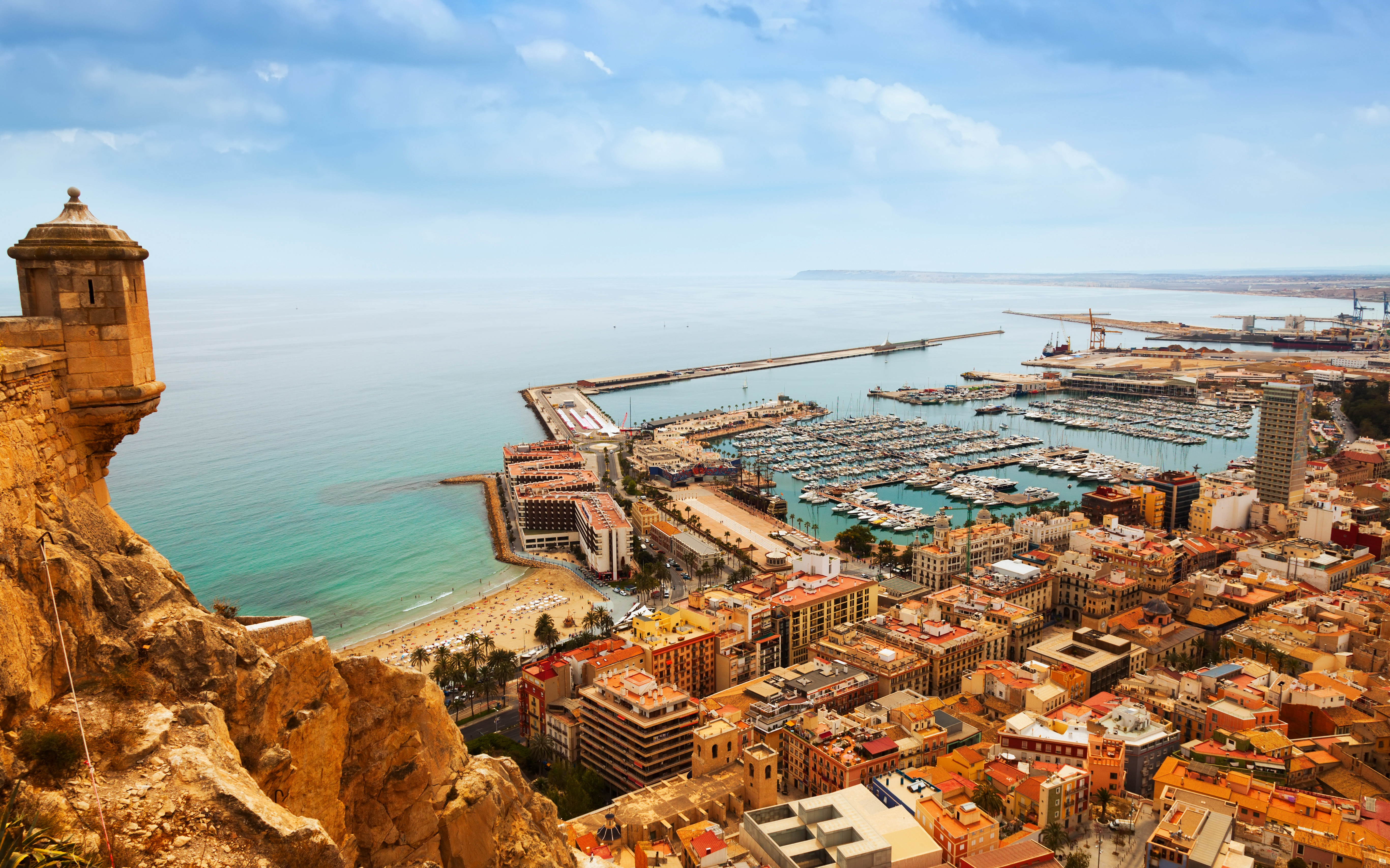 Aerial view of Alicante, Spain, showcasing Santa Barbara Castle, a bustling marina, and the Mediterranean coastline under a clear sky