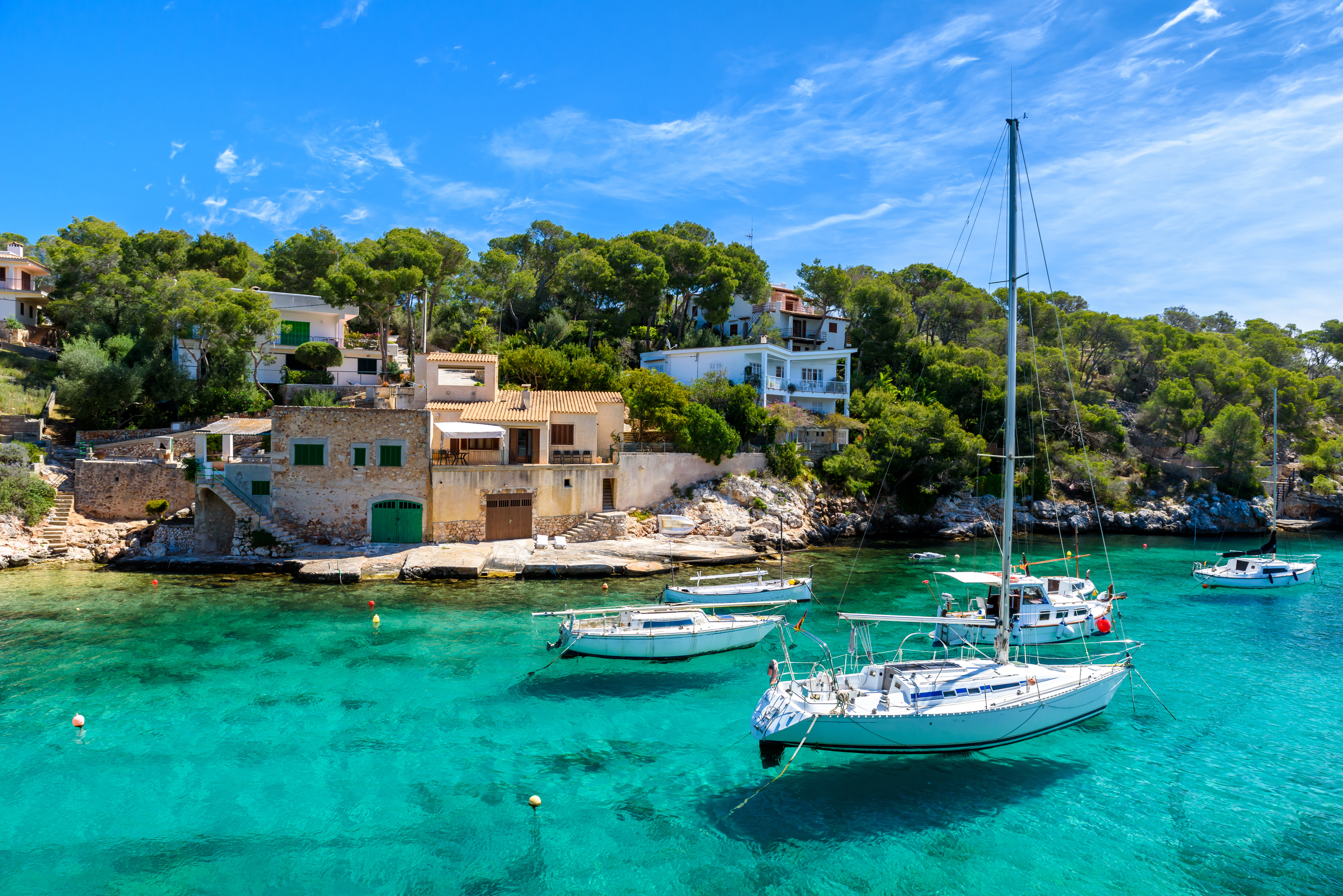 Sailboats anchored in a picturesque bay with turquoise waters and lush greenery, in front of charming Mediterranean villas
