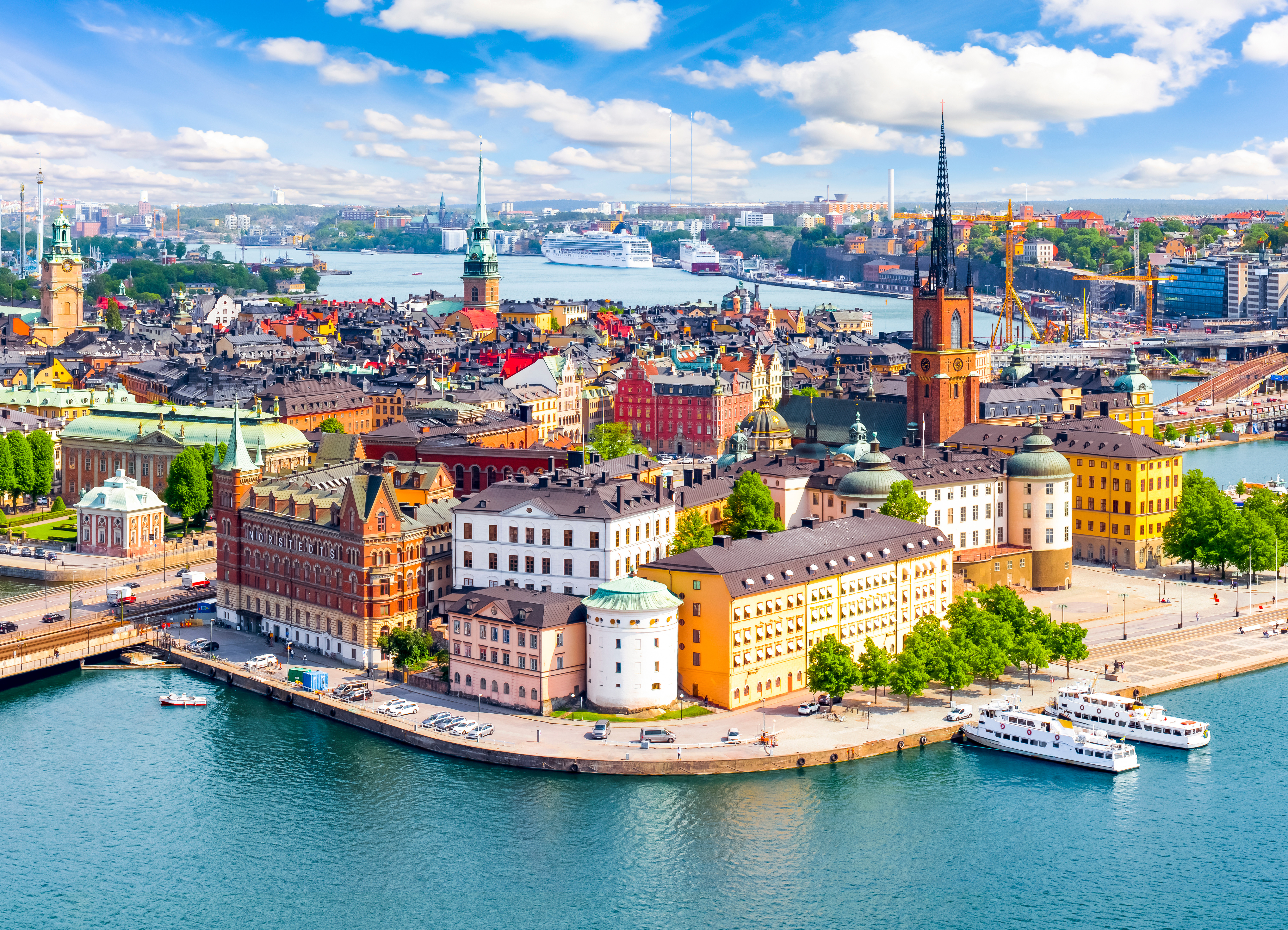 Scenic view of Stockholm's waterfront featuring historic buildings, churches, and boats under a partly cloudy sky