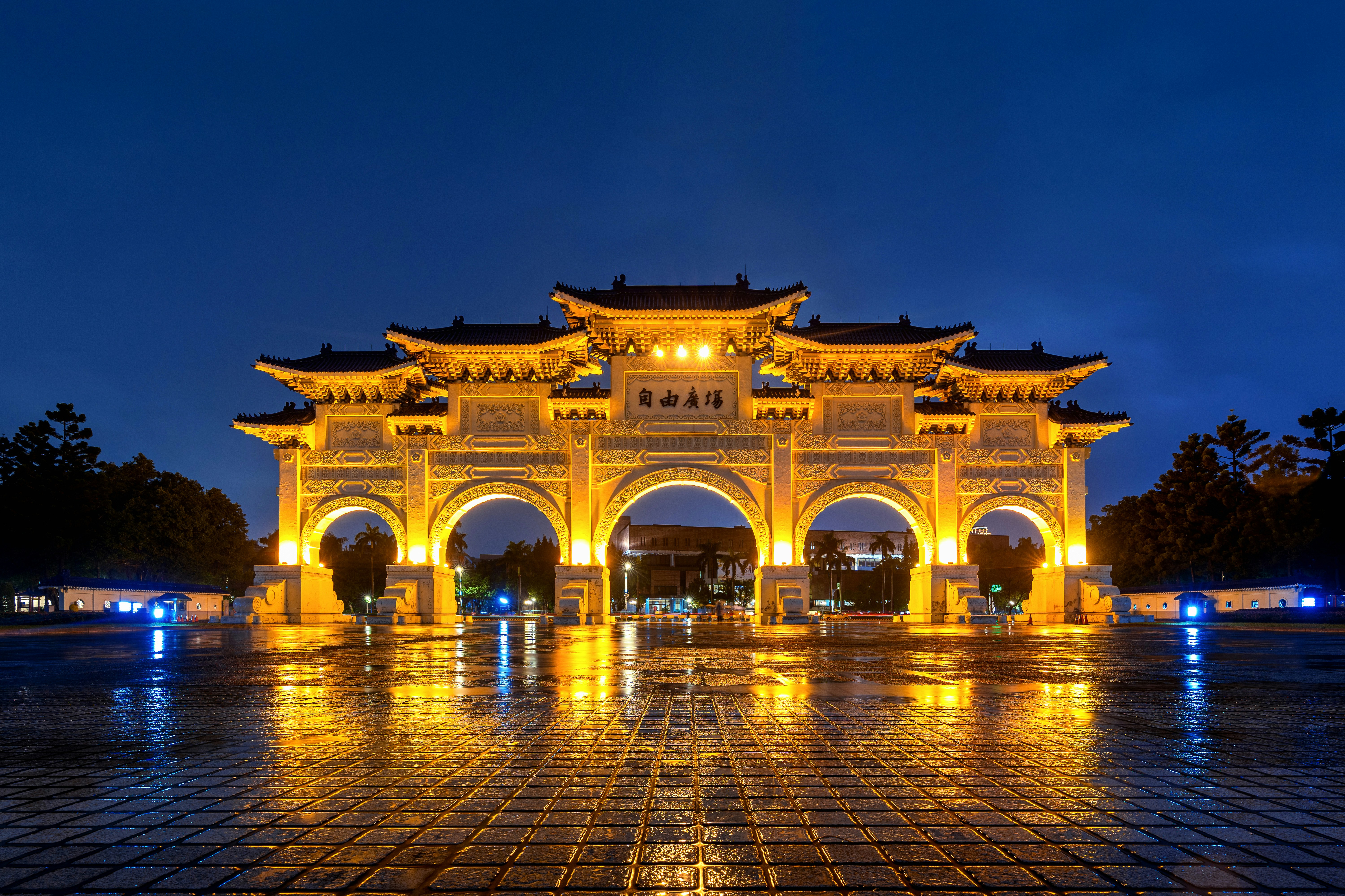 Illuminated Liberty Square Arch in Taipei, Taiwan at night, showcasing traditional Chinese architecture with vibrant lighting reflecing on the wet pavement