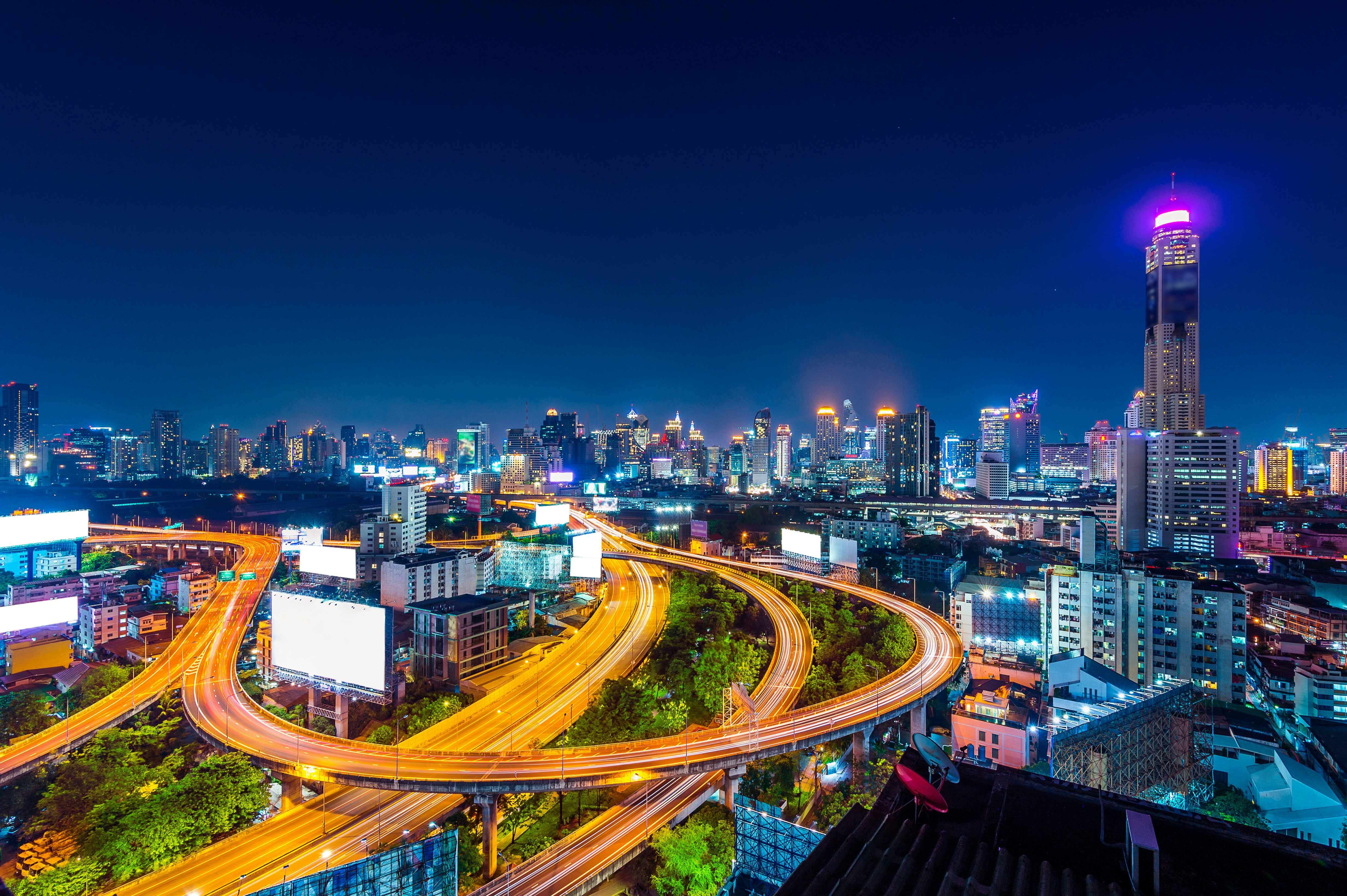 Nighttime cityscape featuring illuminated highways and skyscrapers in Bangkok, Thailand.