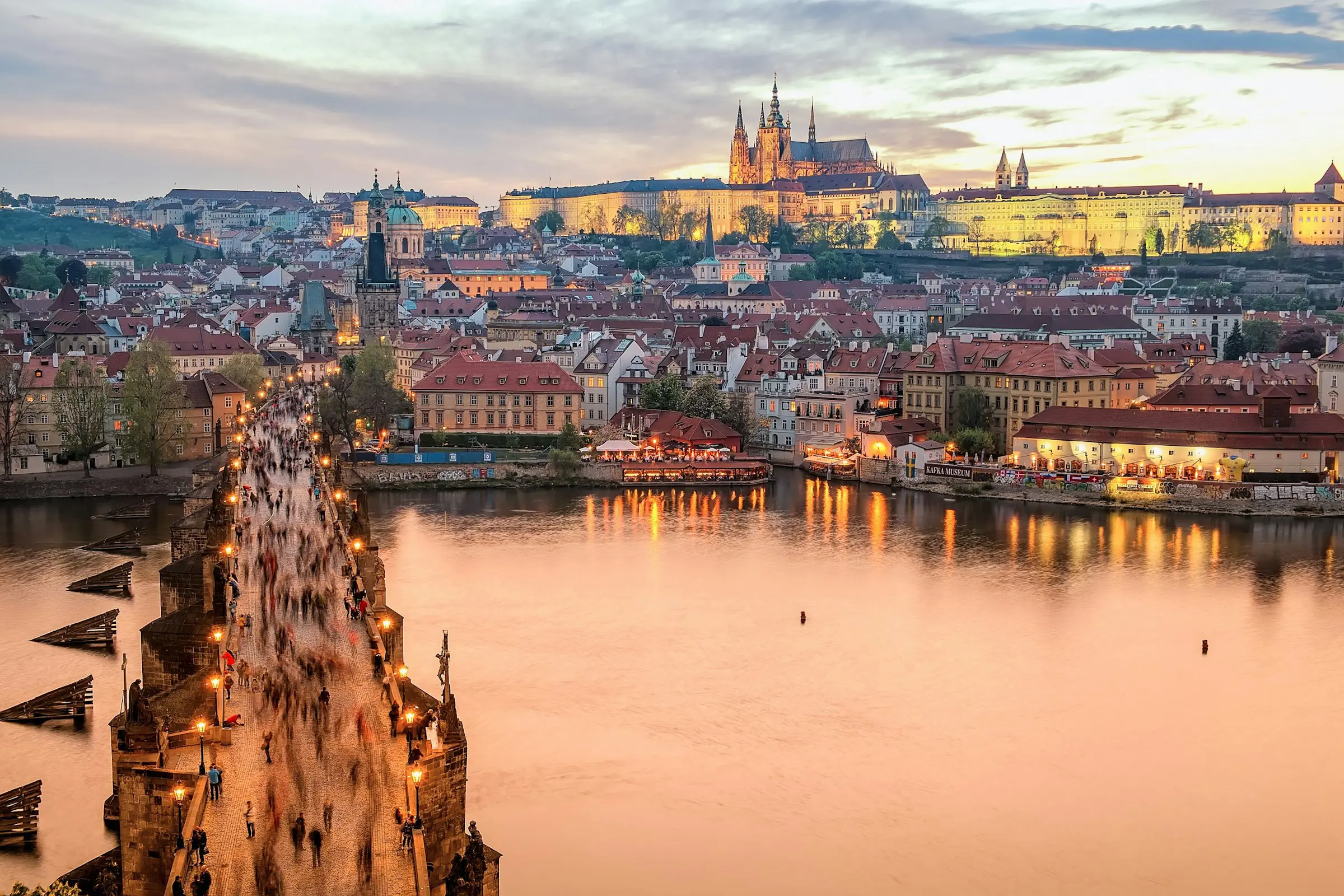 Skymning över Prag med en flod och karlsbron som går över till en stadsdel med slott i bakgrunden