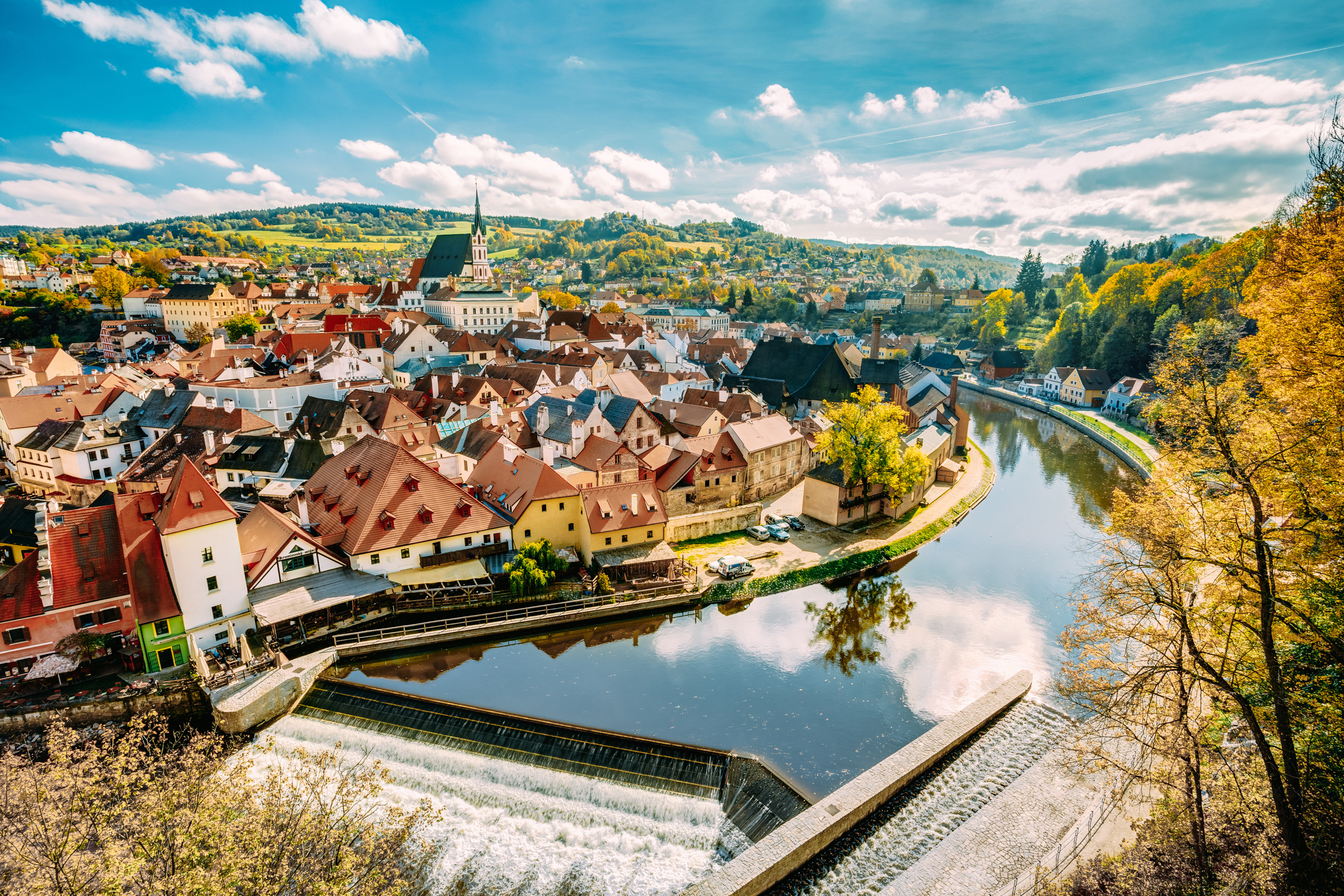 Panoramic view of Český Krumlov, a historic town in the Czech Republic, featuring charming medieval architecture, the Vltava River, and lush autumn foliage under a blue sky