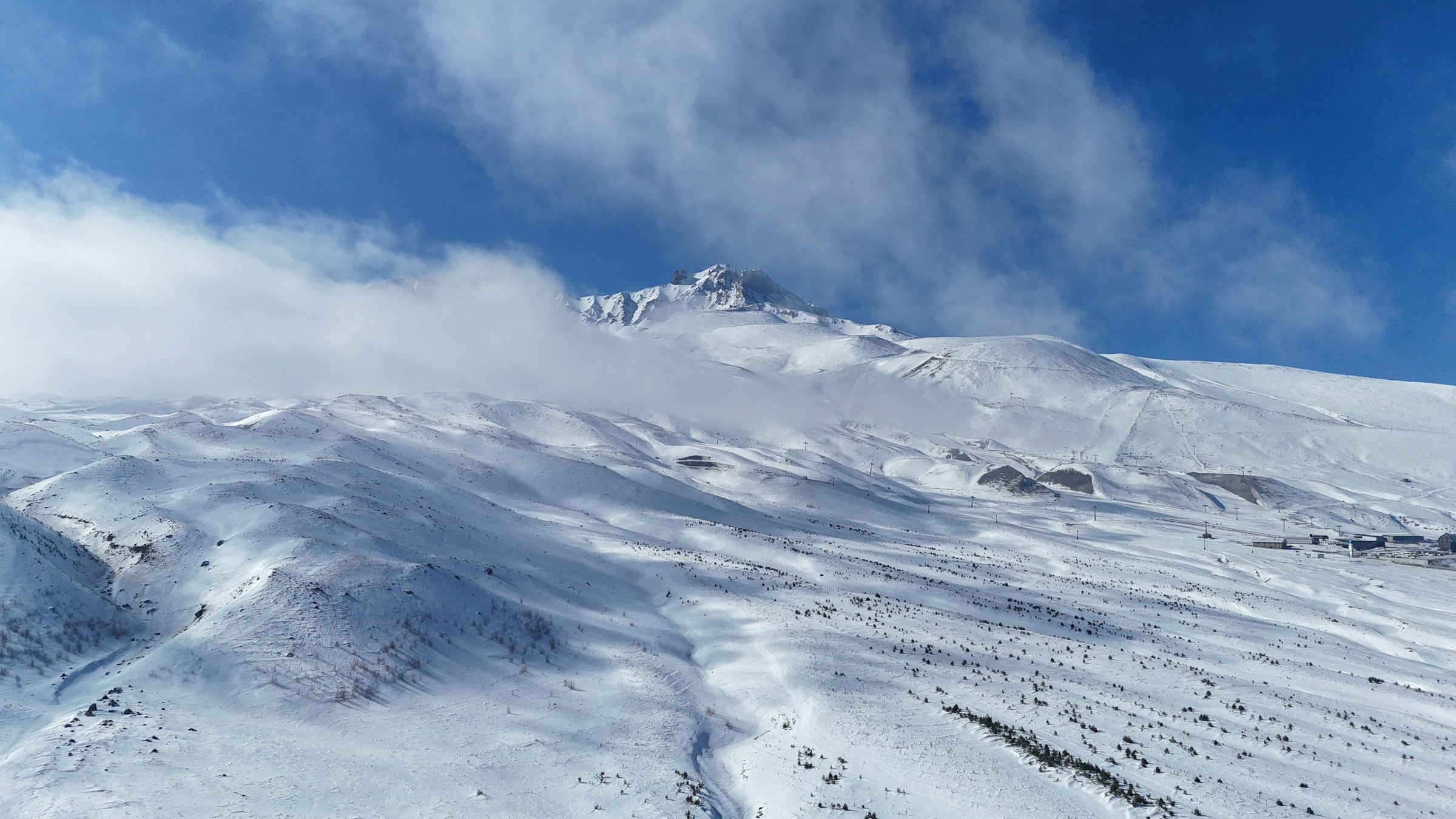 Snöklädda berg under en klarblå himmel med moln vid bergstoppen i Erciyes, Turkiet.