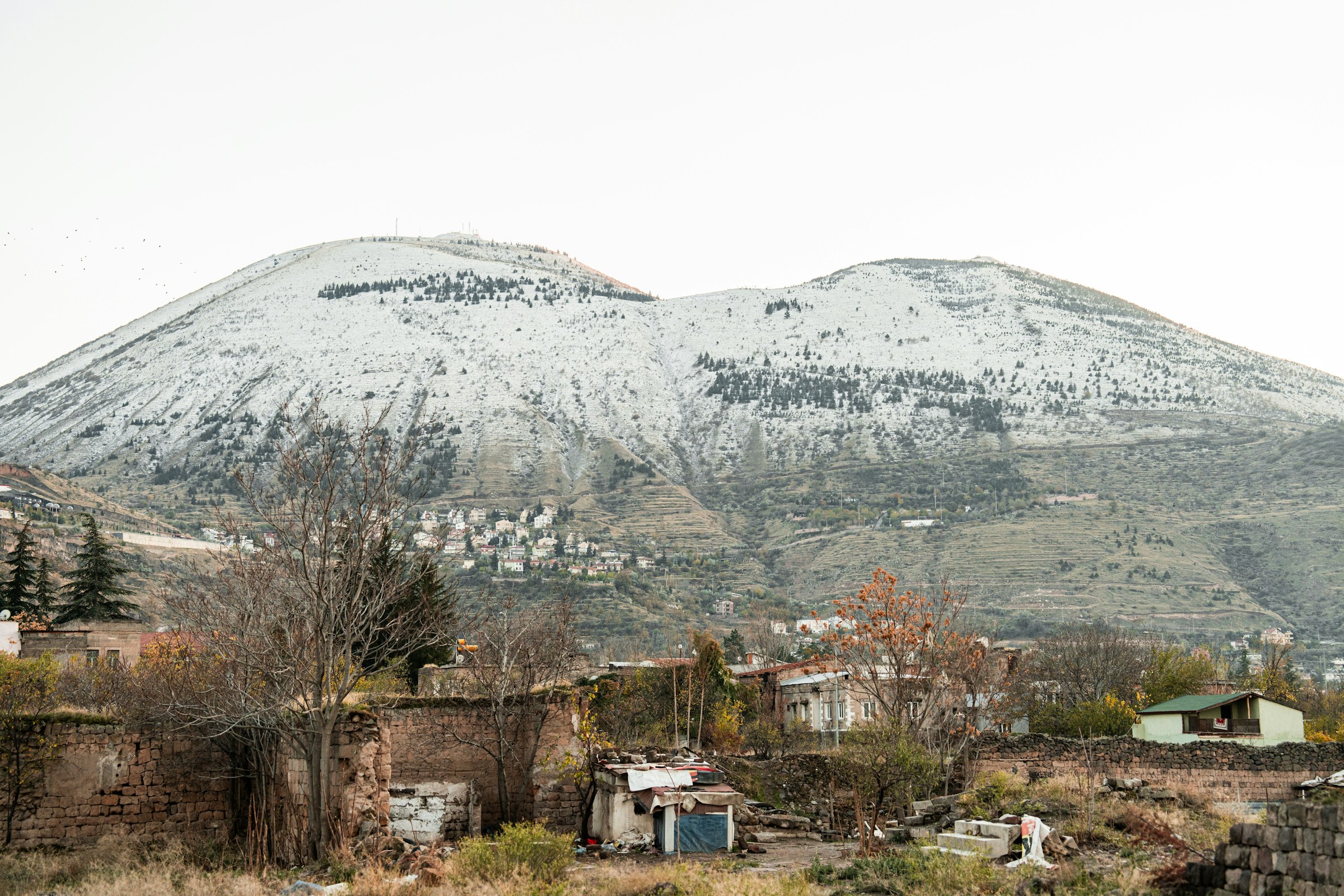 Snötäckt berglandskap med små hus och träd i förgrunden, sedd vid basen av berget Erciyes.