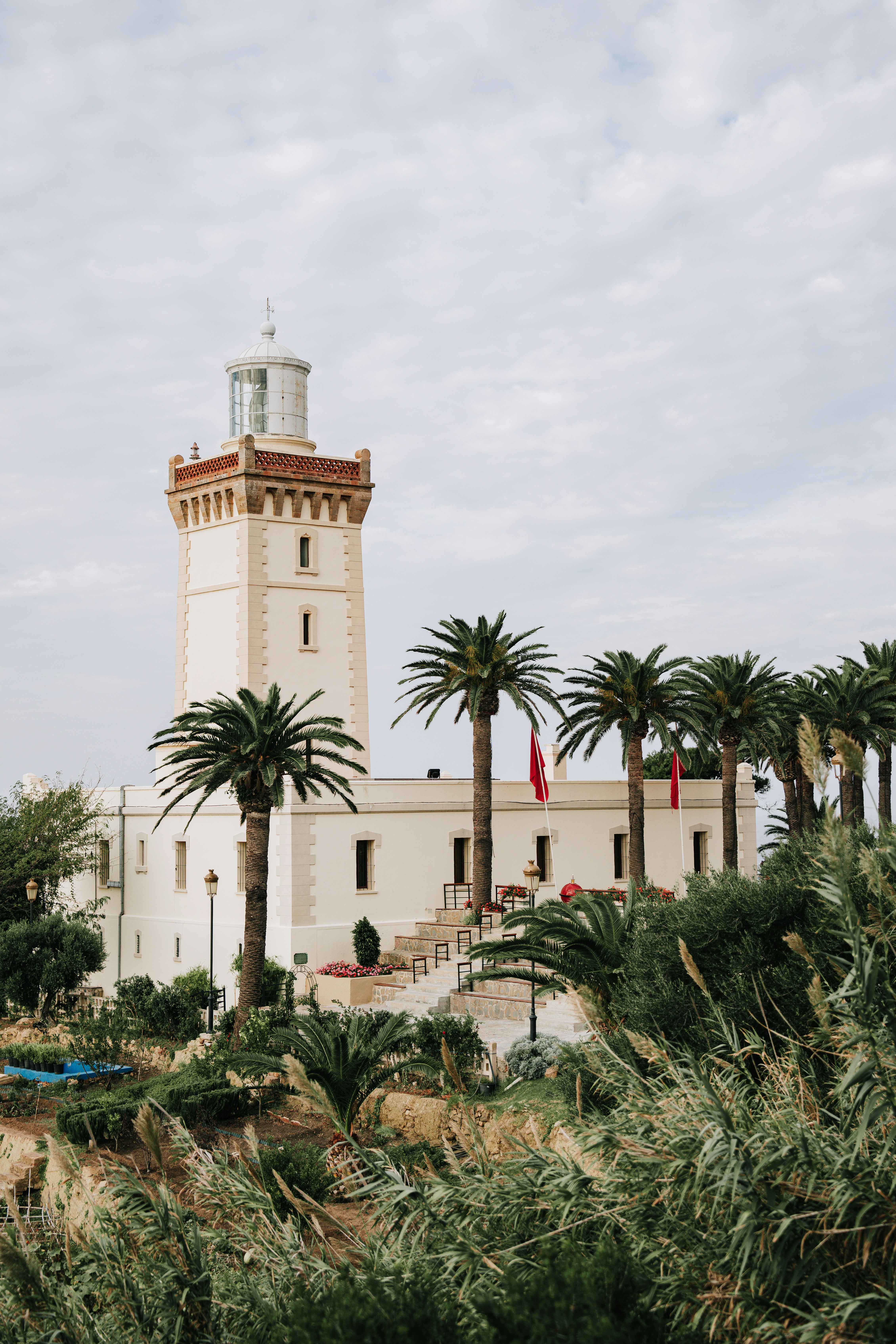 Vit fyr med vakttorn flankerad av palmer och grönskande buskage framför en klar himmel i Tunisien, Turkiet.