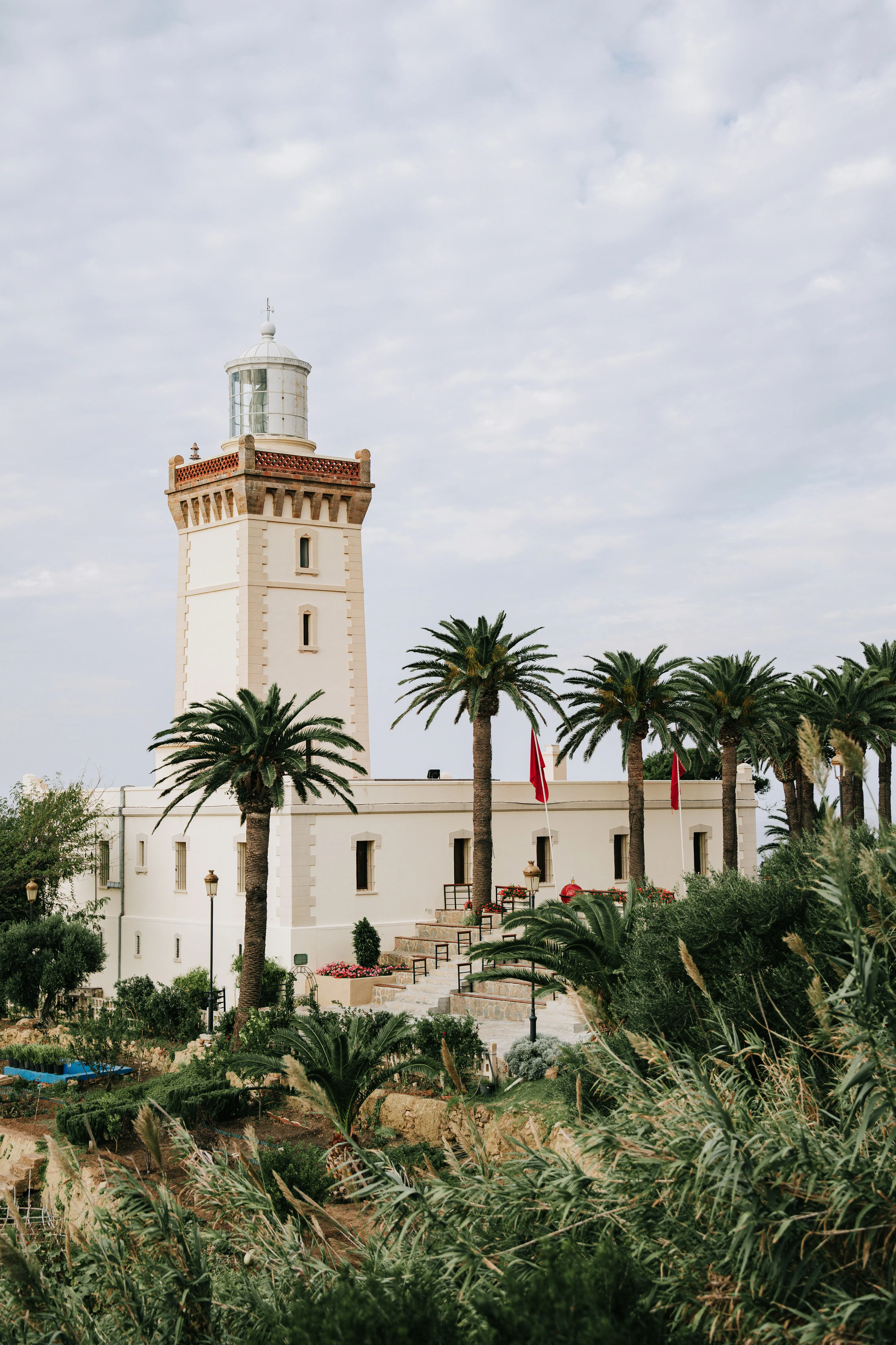 Vit fyr med vakttorn flankerad av palmer och grönskande buskage framför en klar himmel i Tunisien, Turkiet.