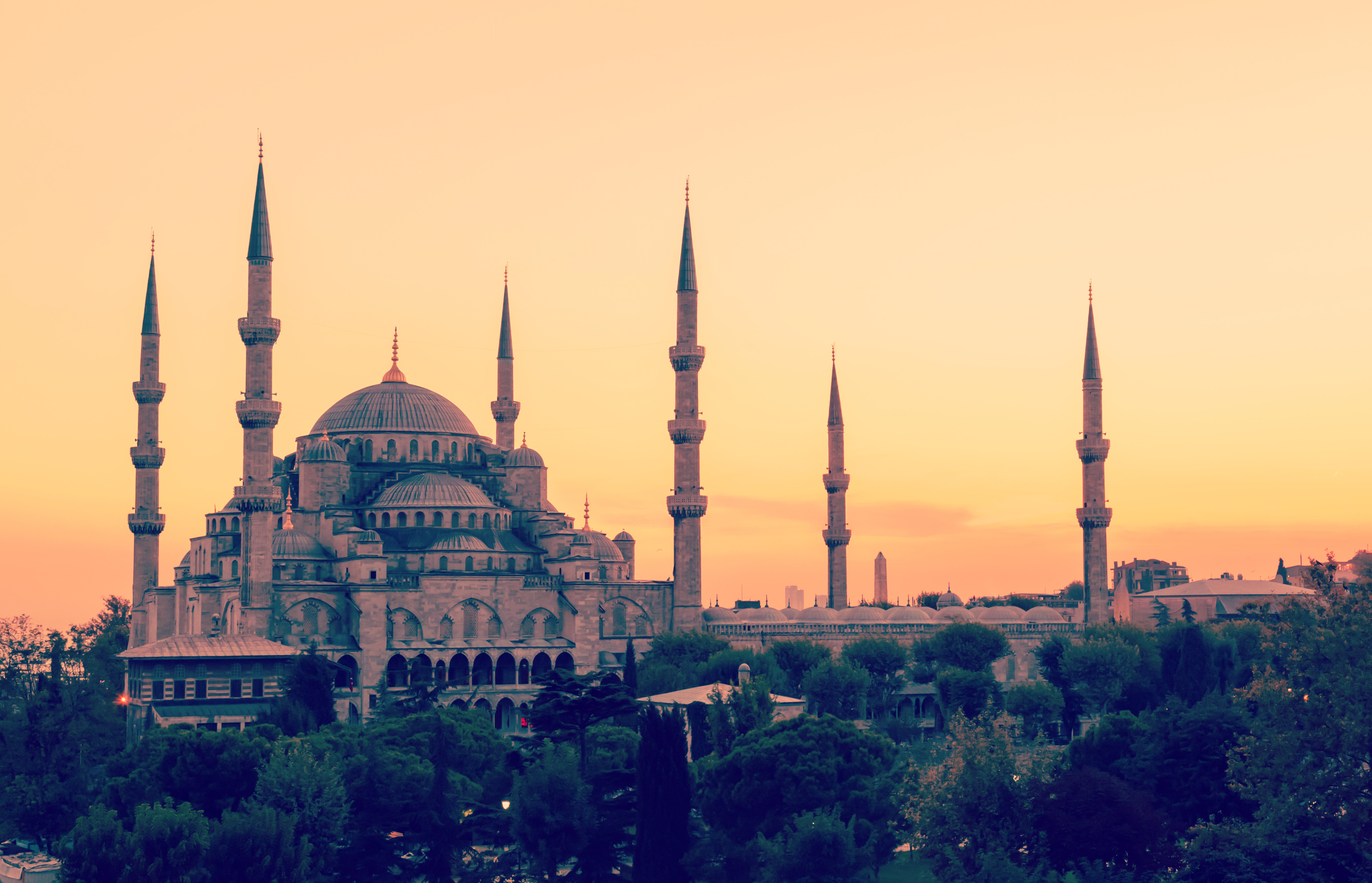 The Blue Mosque in Istanbul at sunset, showcasing its domes and minarets against an orange sky