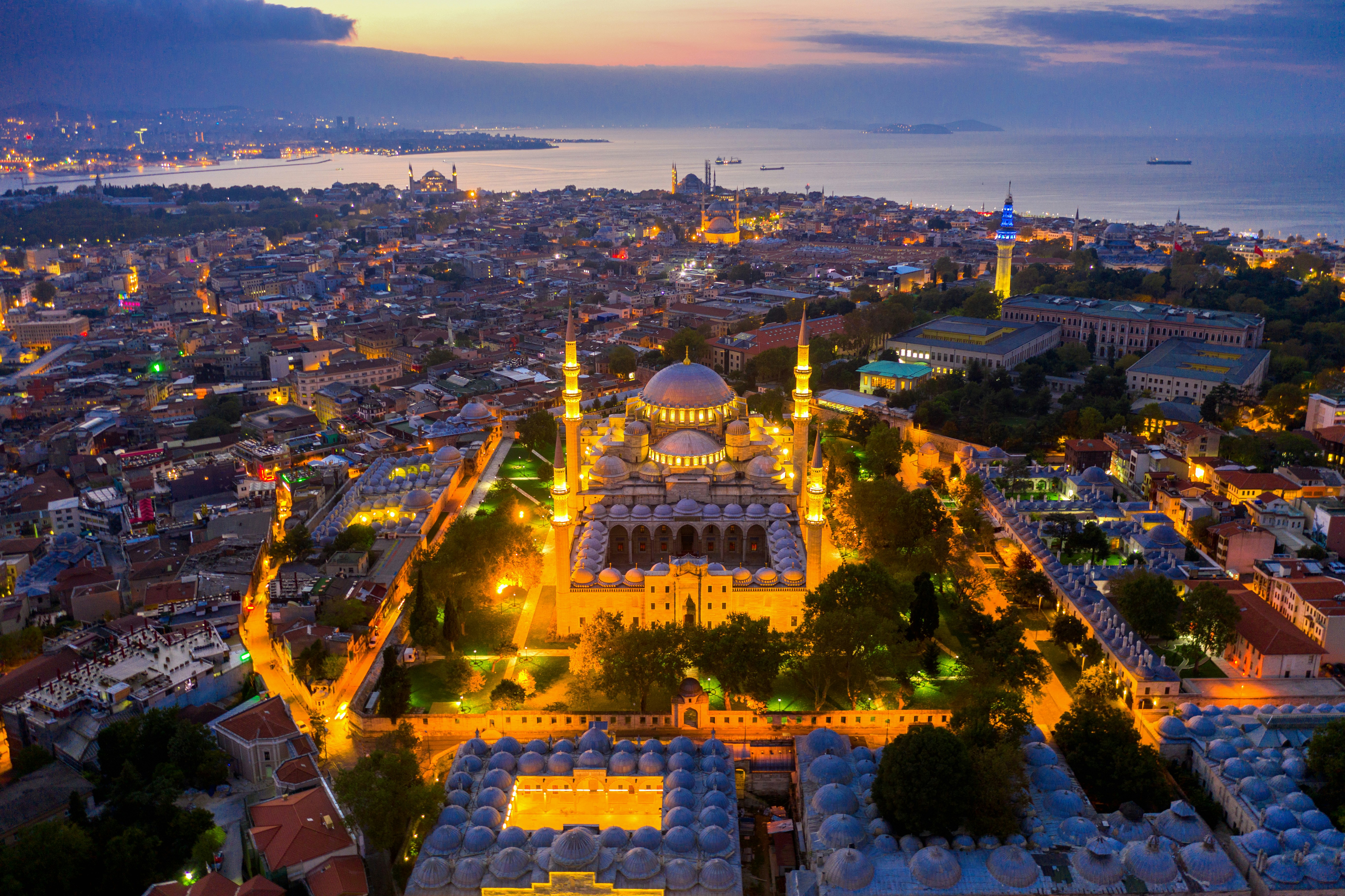 Aerial view of Istanbul at sunset featuring illuminated mosques, vibrant cityscape, and the Bosphorus Strait in the background