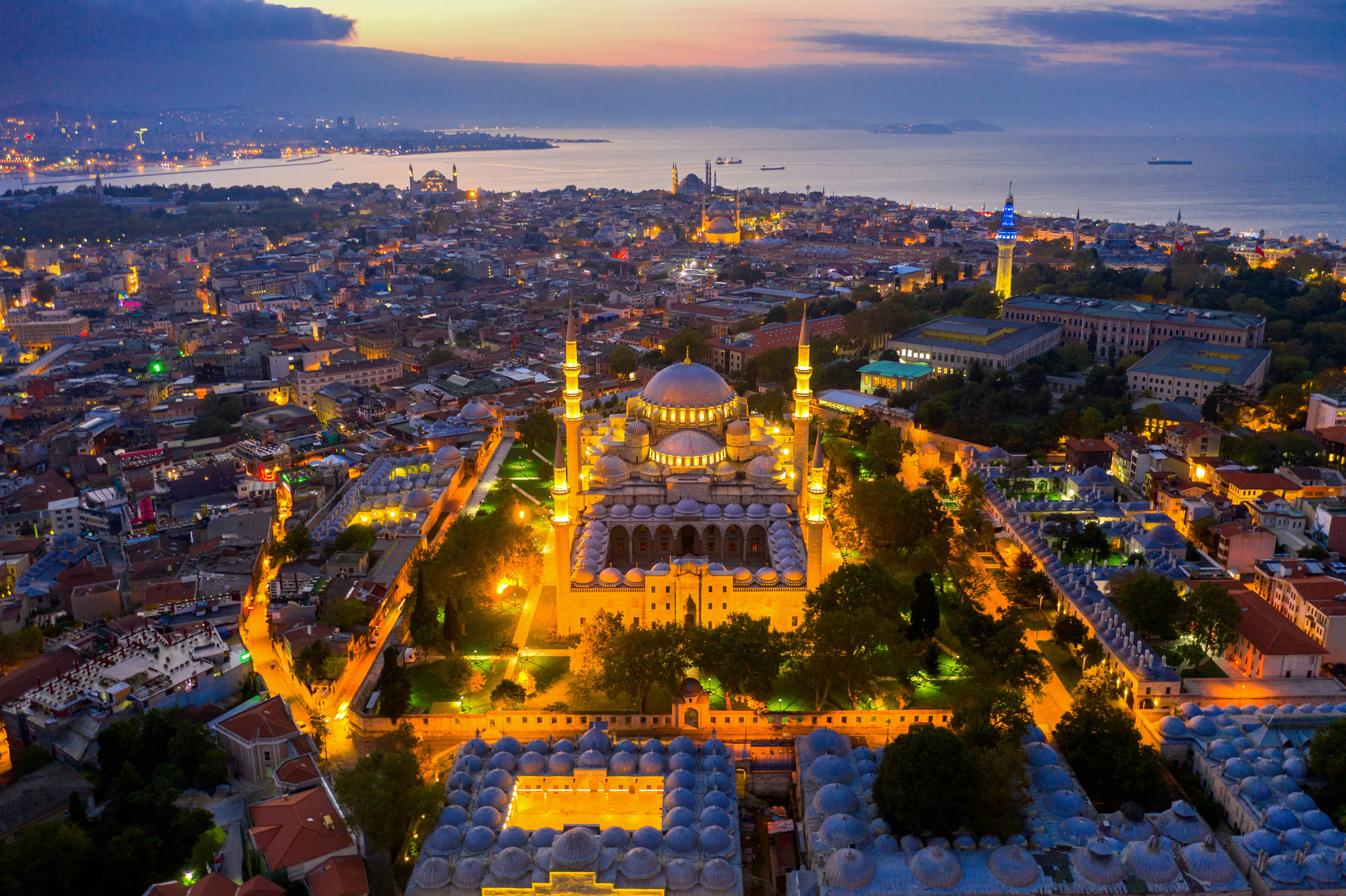 Aerial view of Istanbul at sunset featuring illuminated mosques, vibrant cityscape, and the Bosphorus Strait in the background