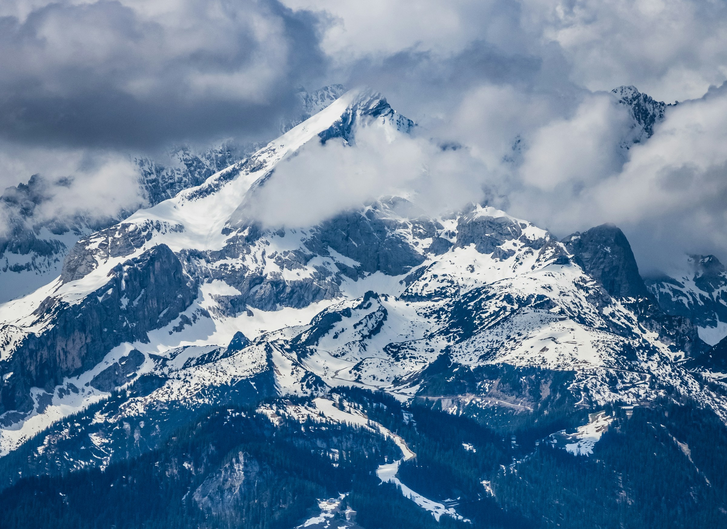 Snow-covered mountain peaks surrounded by clouds and forests