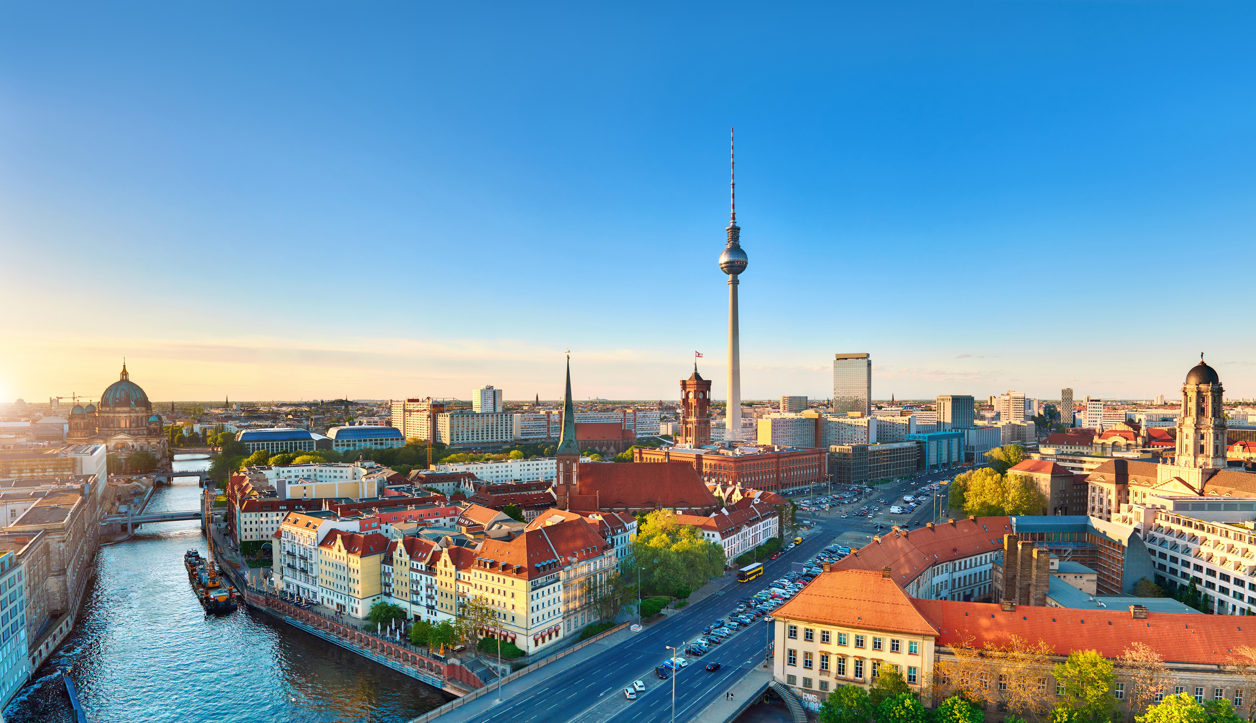 Aerial view of Berlin, Germany at sunset, featuring the iconic Berlin TV Tower and historic buildings along the Spree River under a clear blue sky