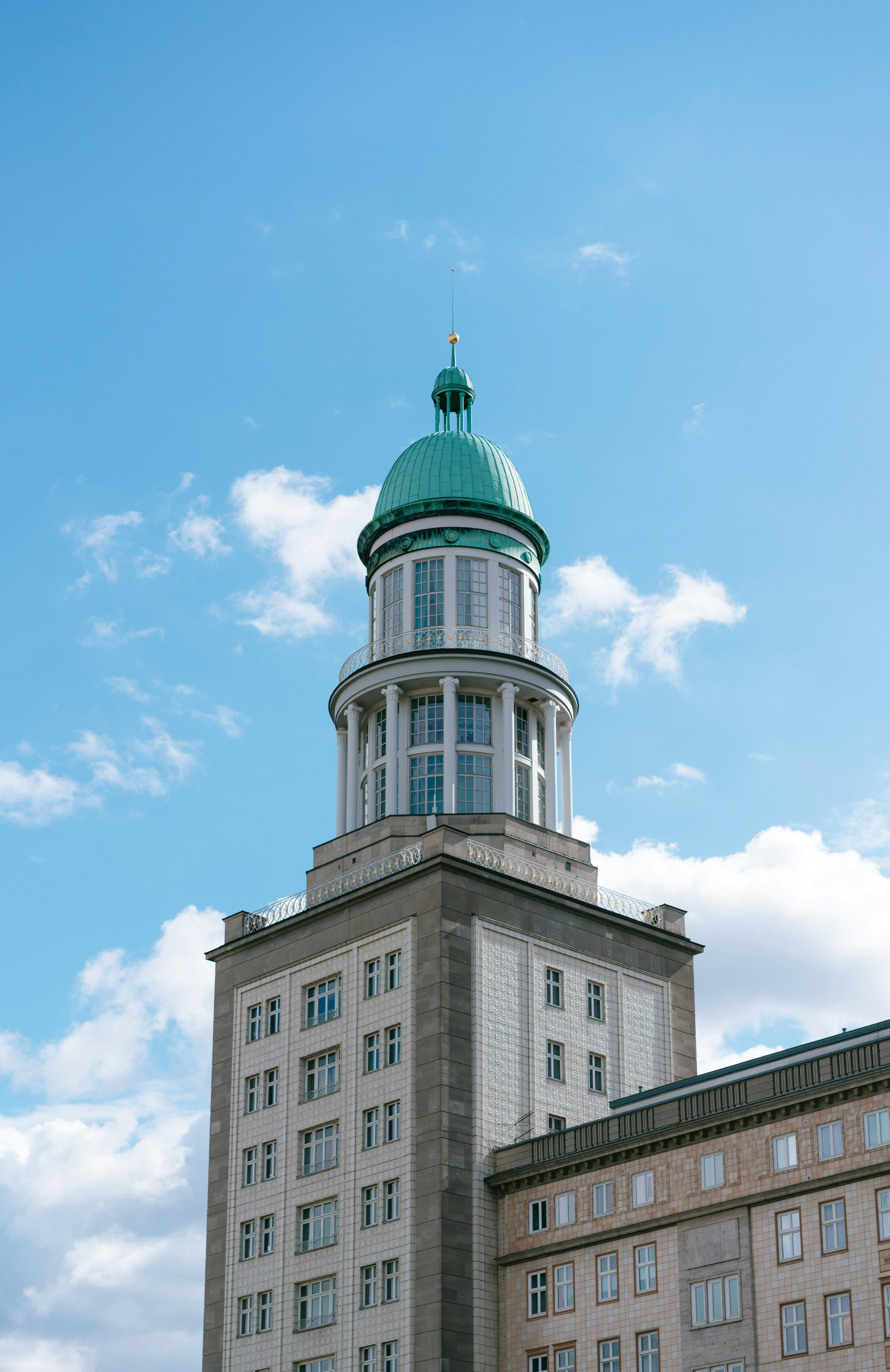 Historic building with green dome against blue sky and clouds, featuring classic architecture and multiple windows