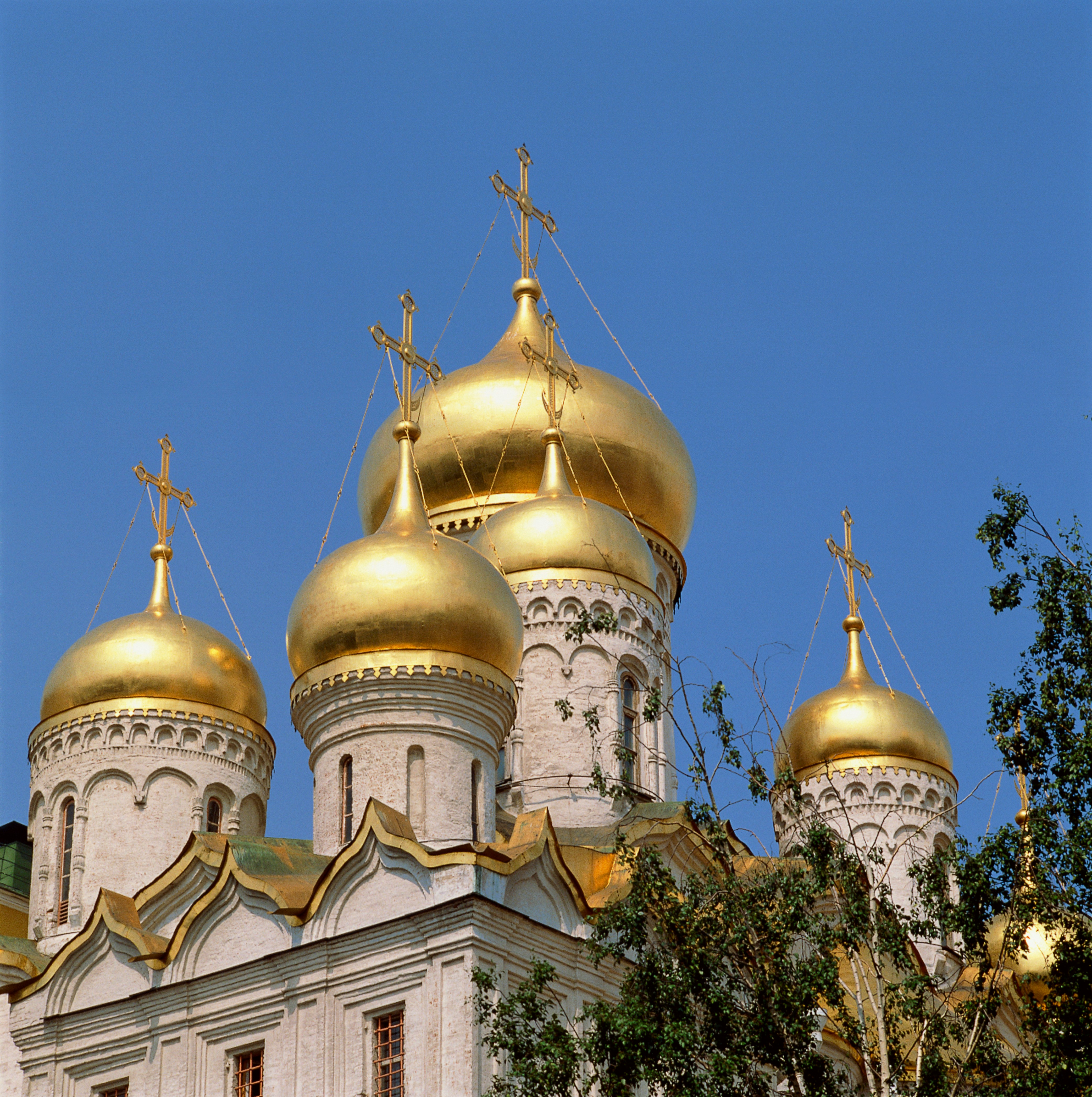 Golden domes of a Russian Orthodox church against a clear blue sky, featuring ornate crosses and detailed architectural elements