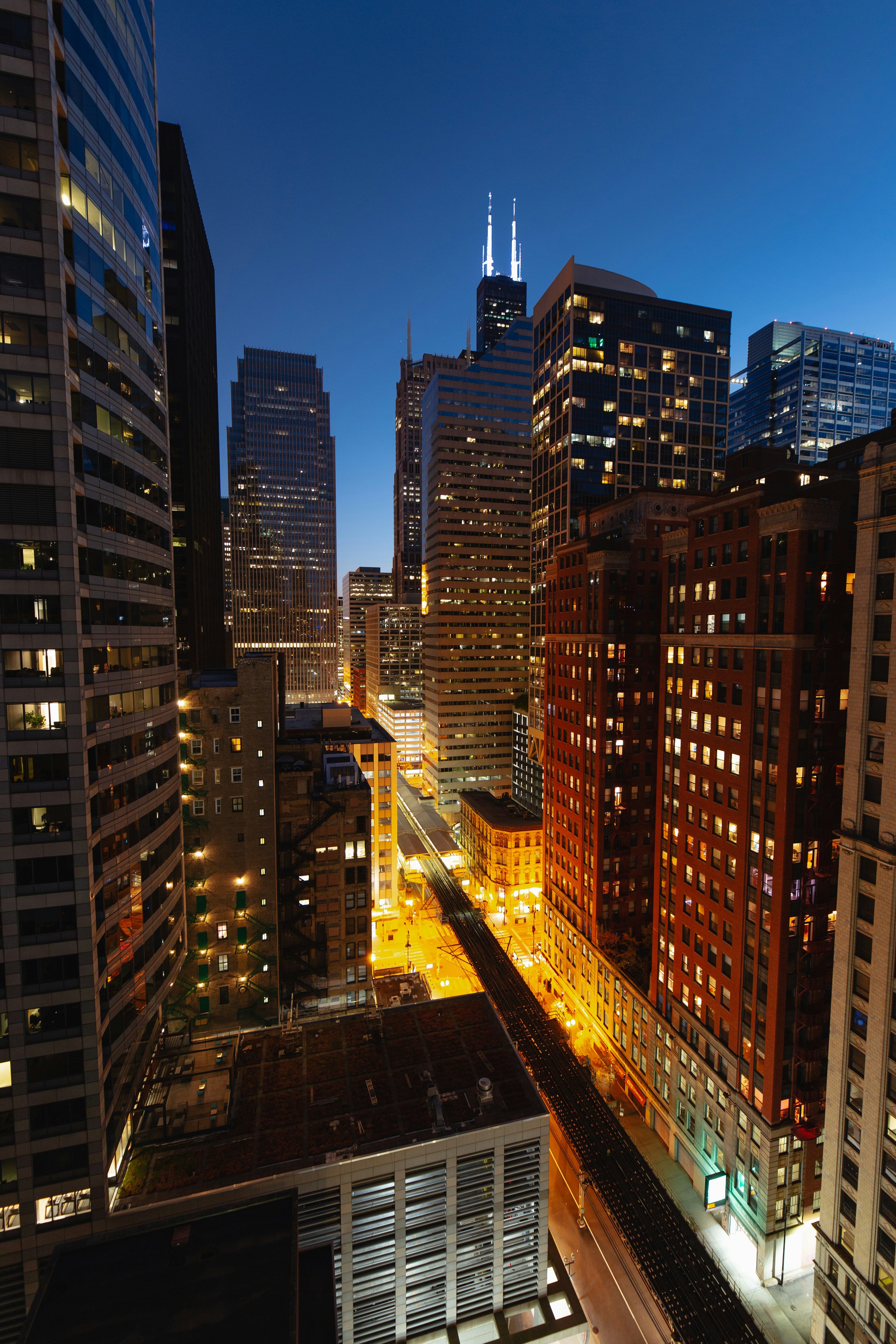 Nighttime view of a vibrant downtown cityscape with illuminated skyscrapers and a clear blue sky