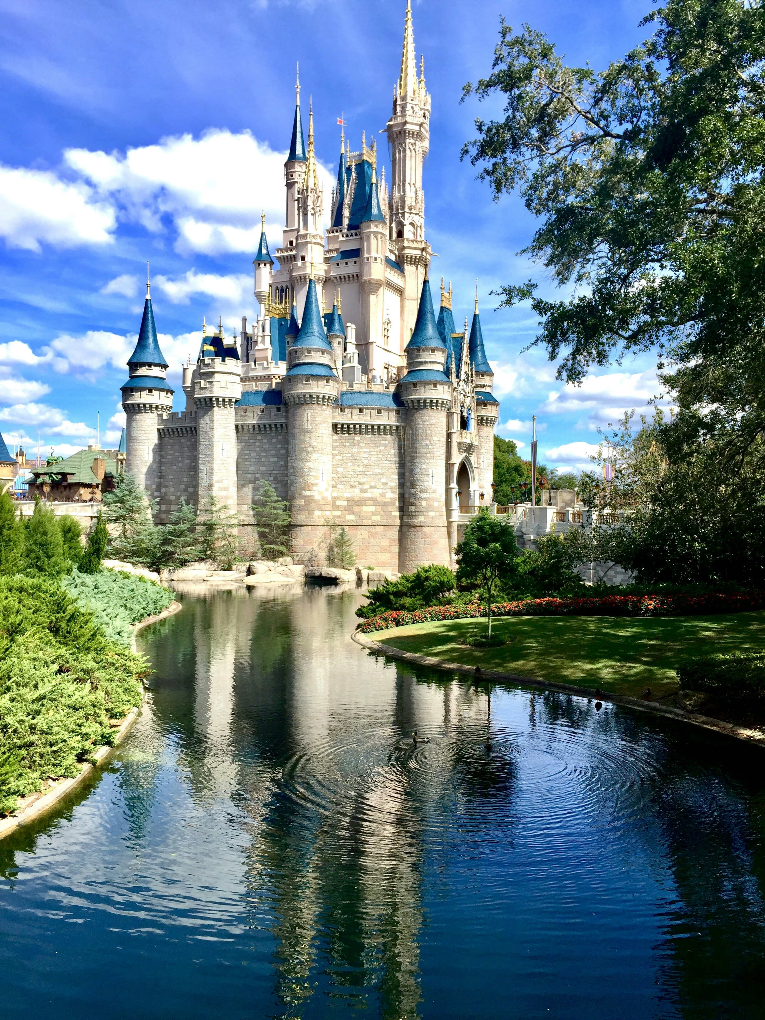 Majestic castle with blue turrets surrounded by a serene moat and lush greenery under a vibrant blue sky