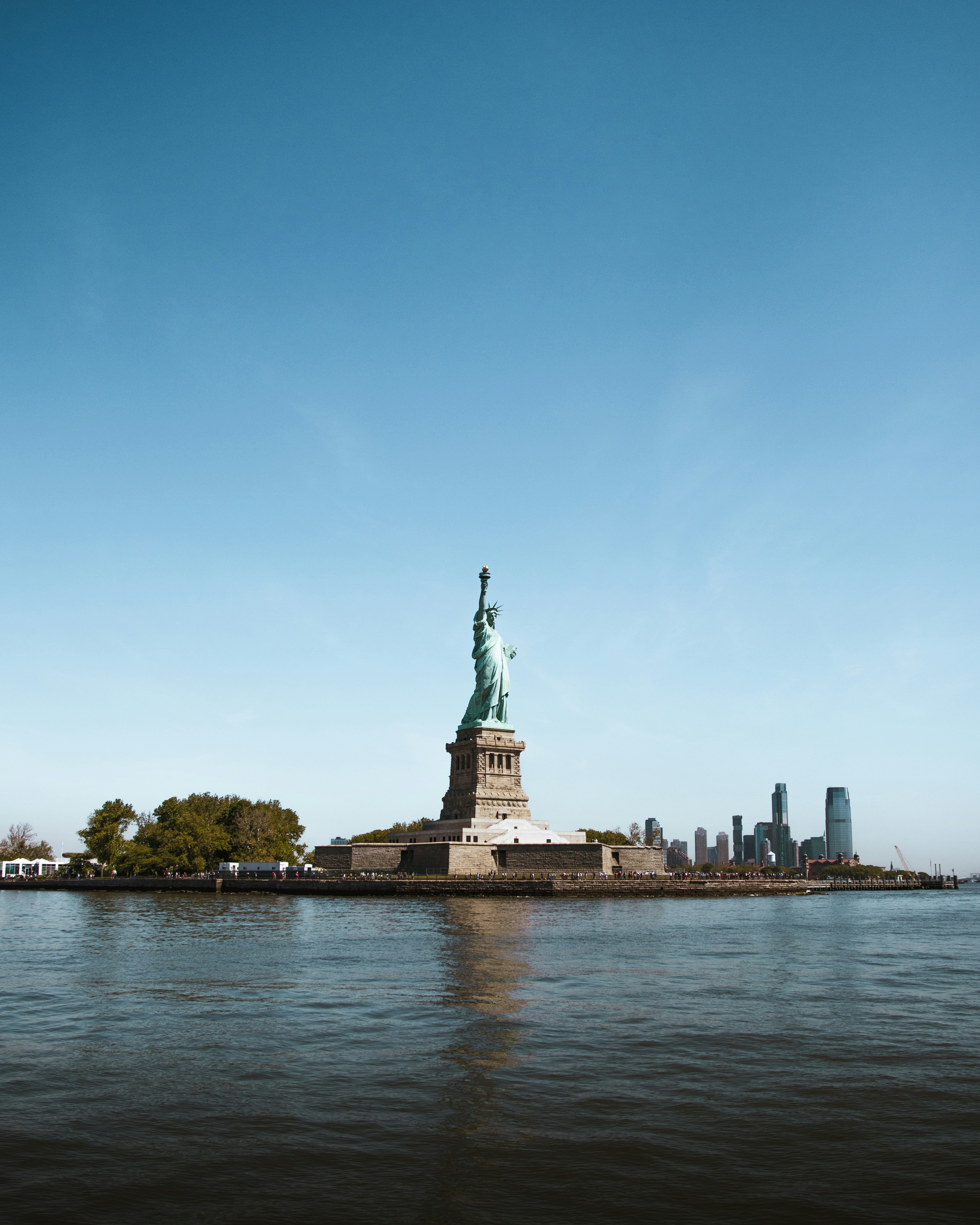 Statue of Liberty on Liberty Island with New York City skyline in the background under a clear blue sky