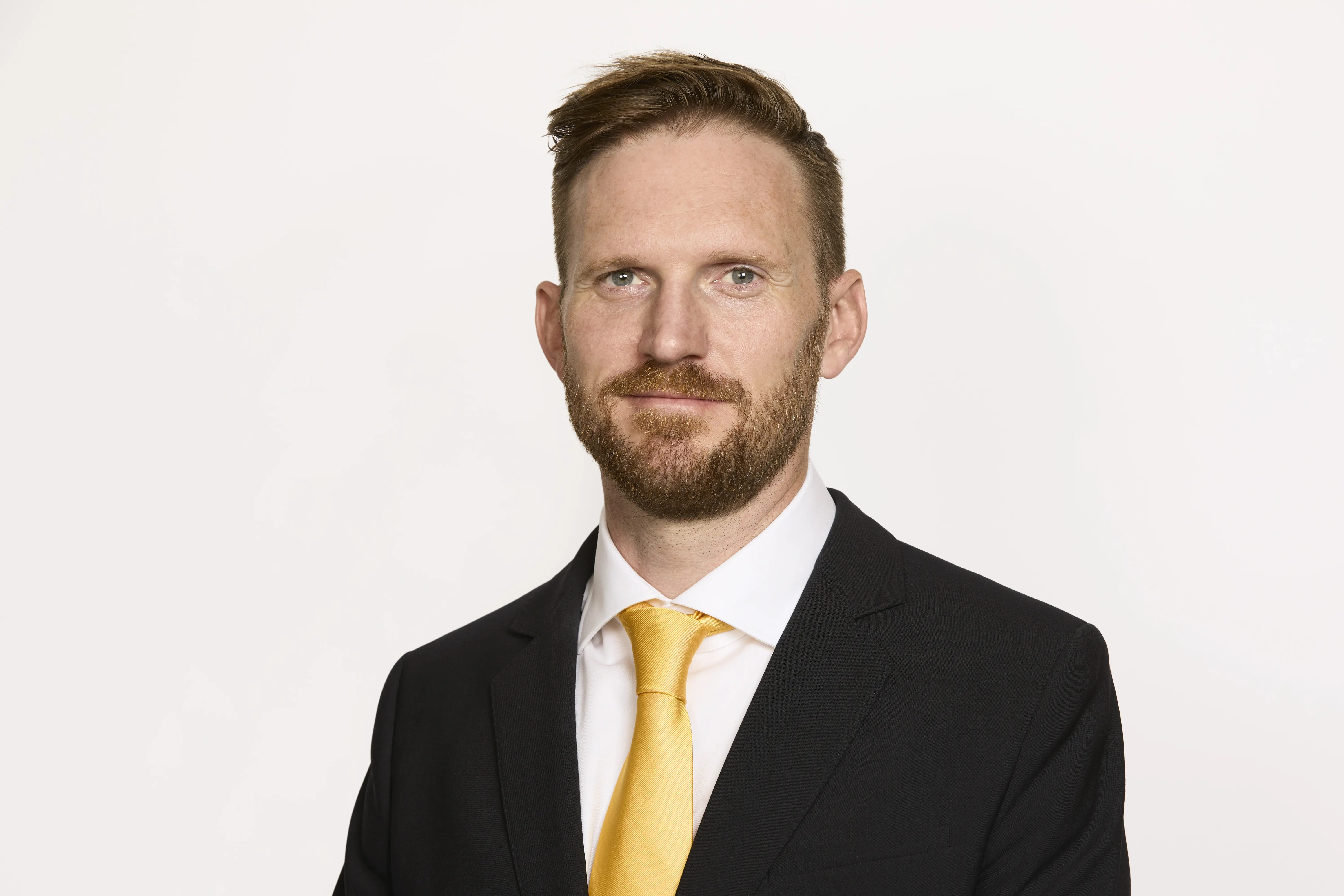 Man i kostym står vänd mot och tittar in i kameran.