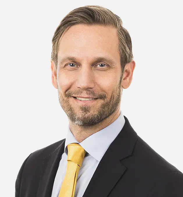 Mårten Barkman - Professionellt porträtt av en leende man i kostym med gul slips mot vit bakgrund.