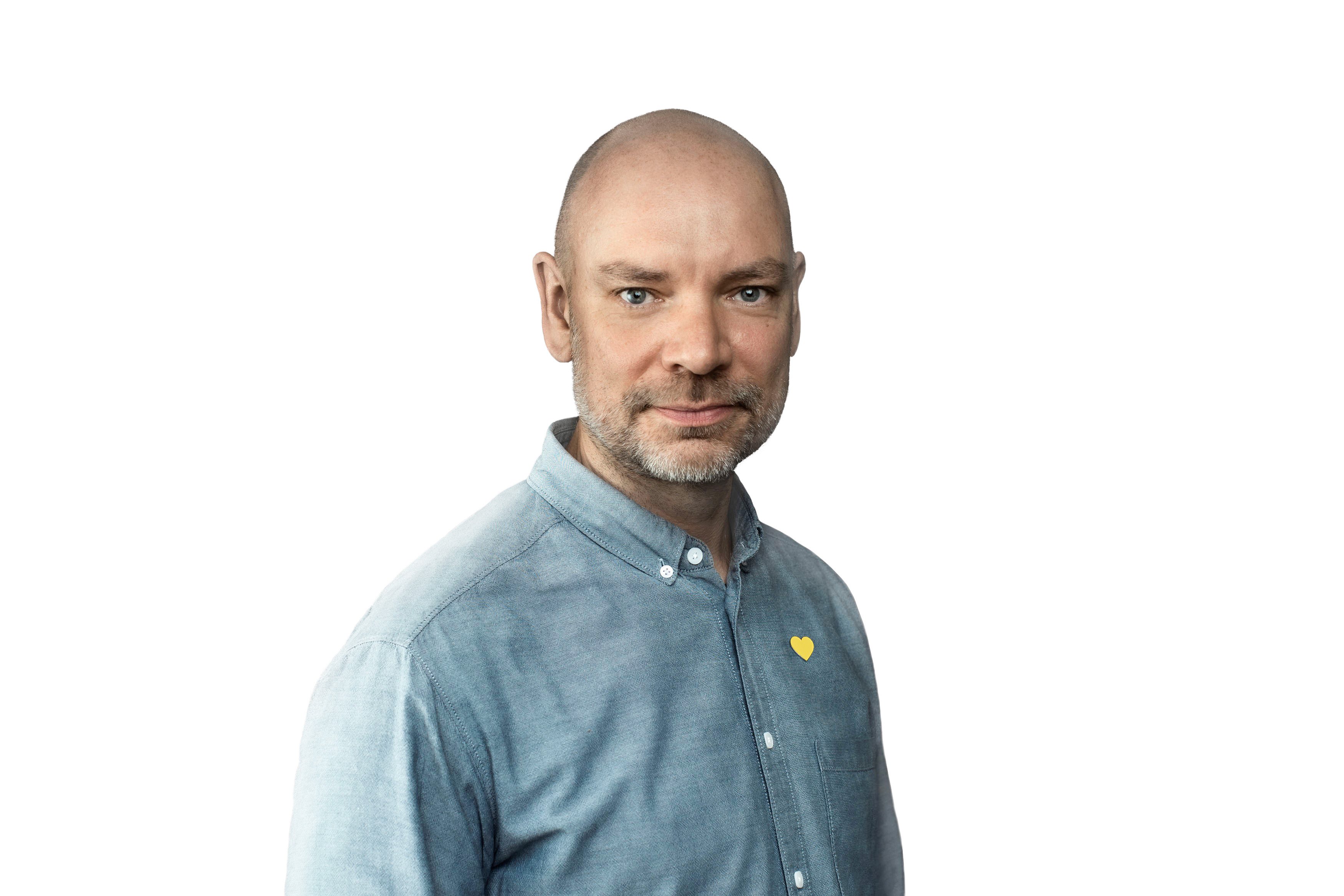 Man i blå skjorta med ett gult hjärta på bröstet, mot en vit bakgrund.