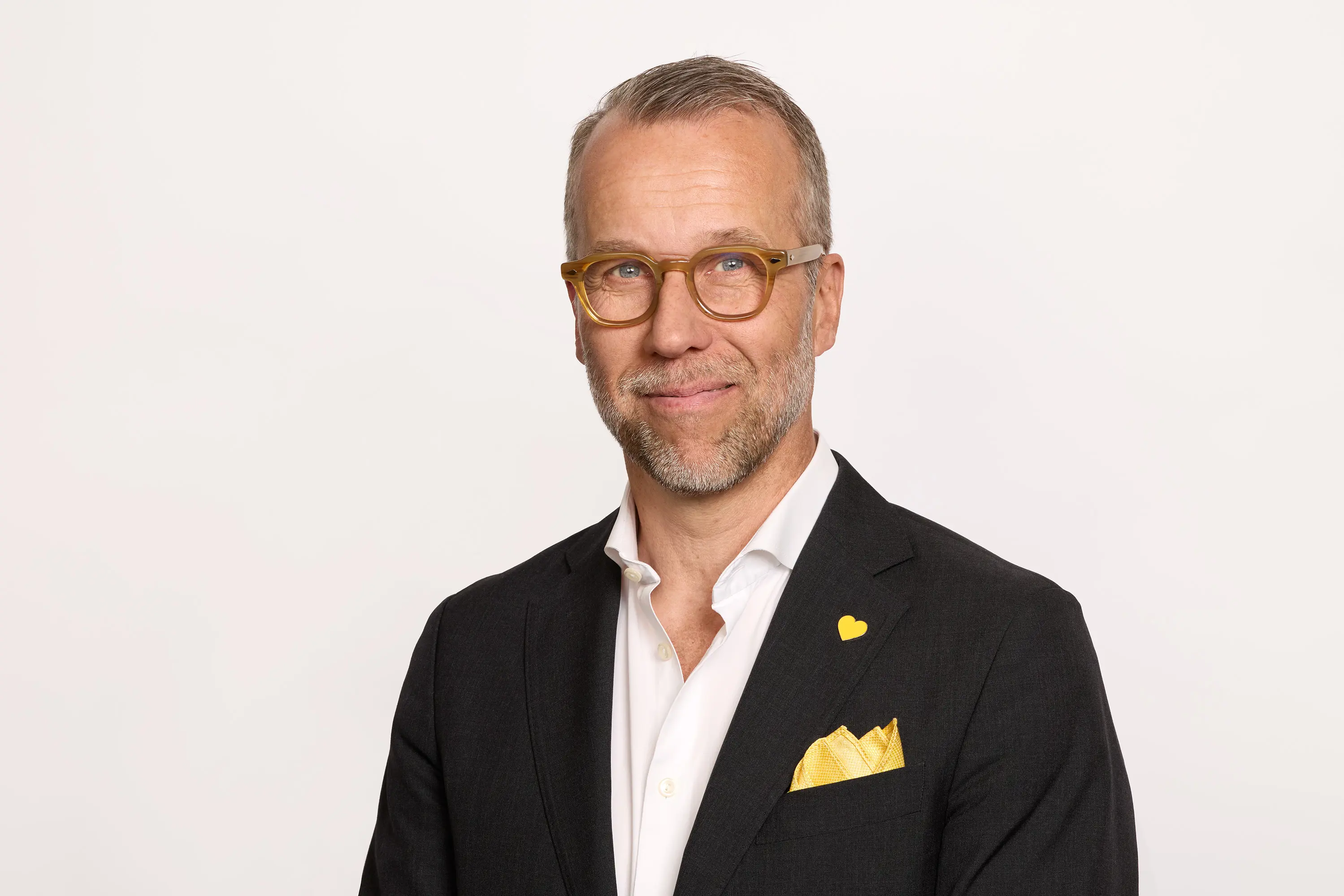 Middle-aged man with glasses and a beard wearing a black suit, white shirt, and yellow pocket square, posed against a plain white background.