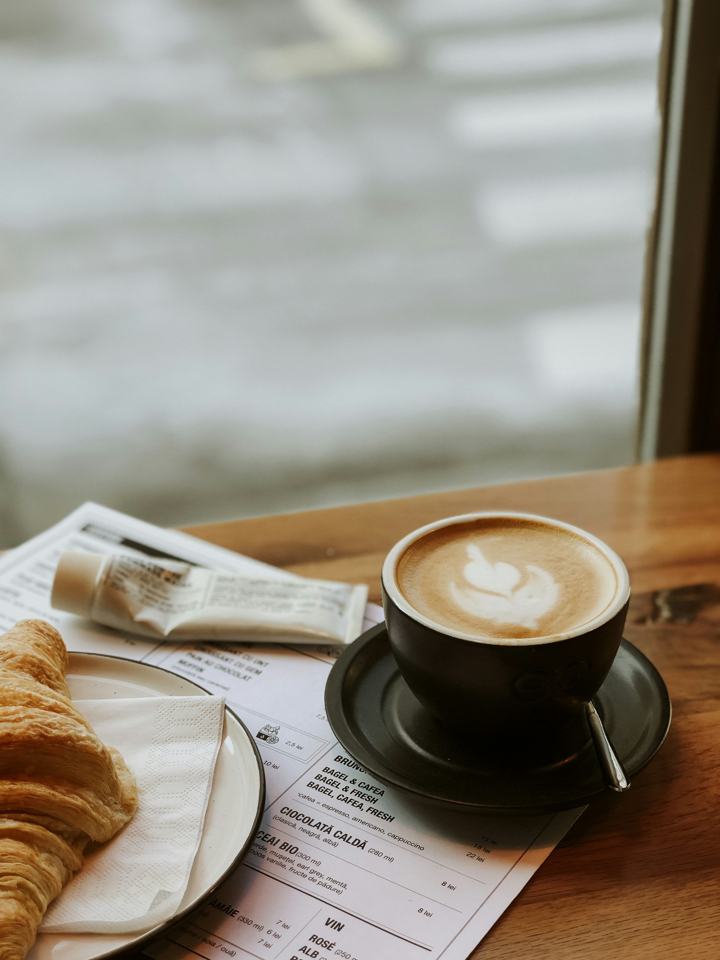  Cappuccino and croissant on wooden table with menu in the background. Perfect for breakfast or coffee in a café.